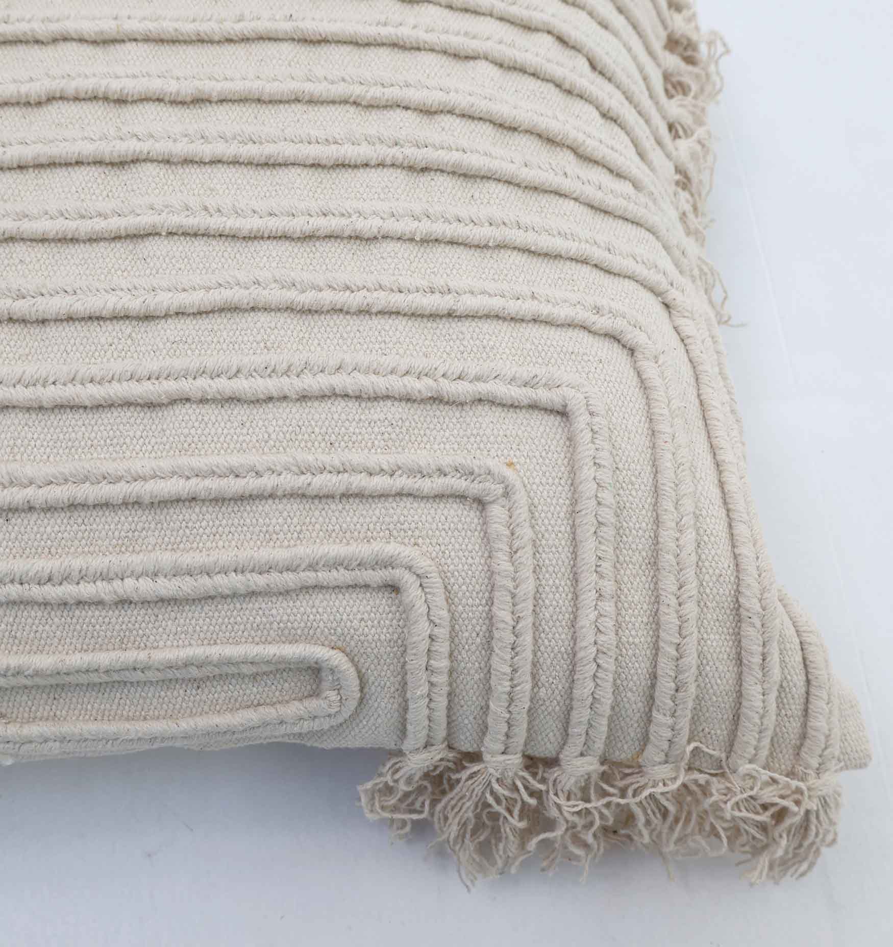 A close-up of Ramsha Home’s Home Decor Cushion Natural Color - CS 302 (45x45cm), featuring raised, looped patterns and fringed edges—an elegant beige accent piece from a luxury home furnishings brand in the UAE.