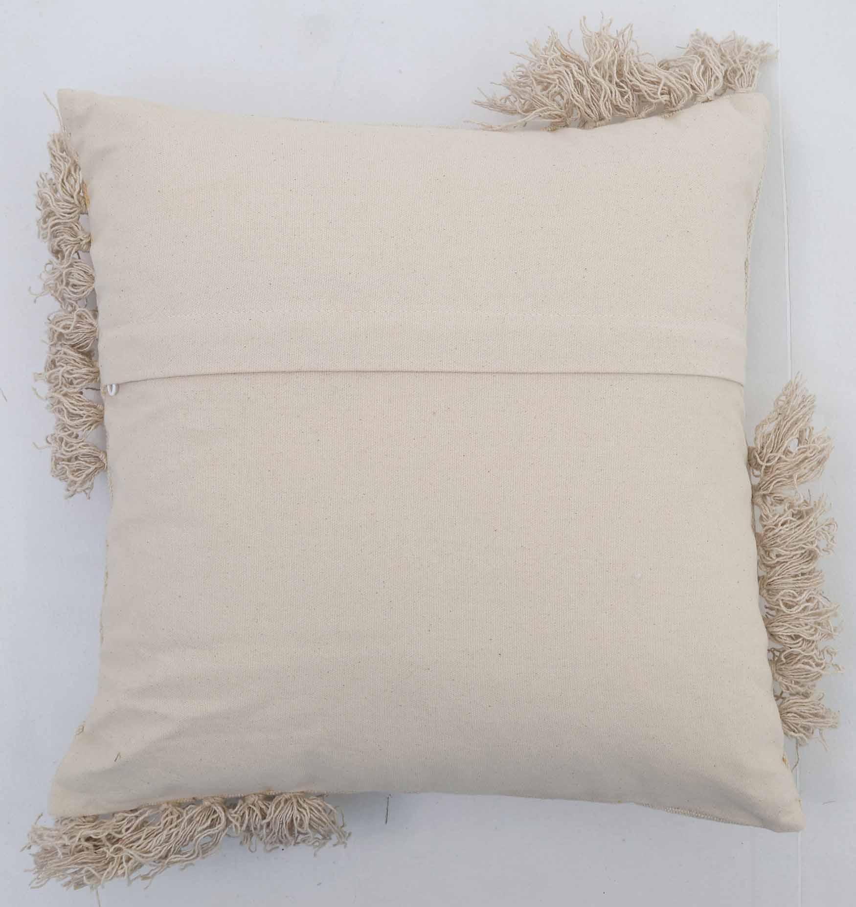 The Home Decor Cushion Natural Color - CS 302 (45x45cm) by Ramsha Home features a plain fabric cover, horizontal back seam, and decorative beige fringe on two edges—perfect for adding style to any space.