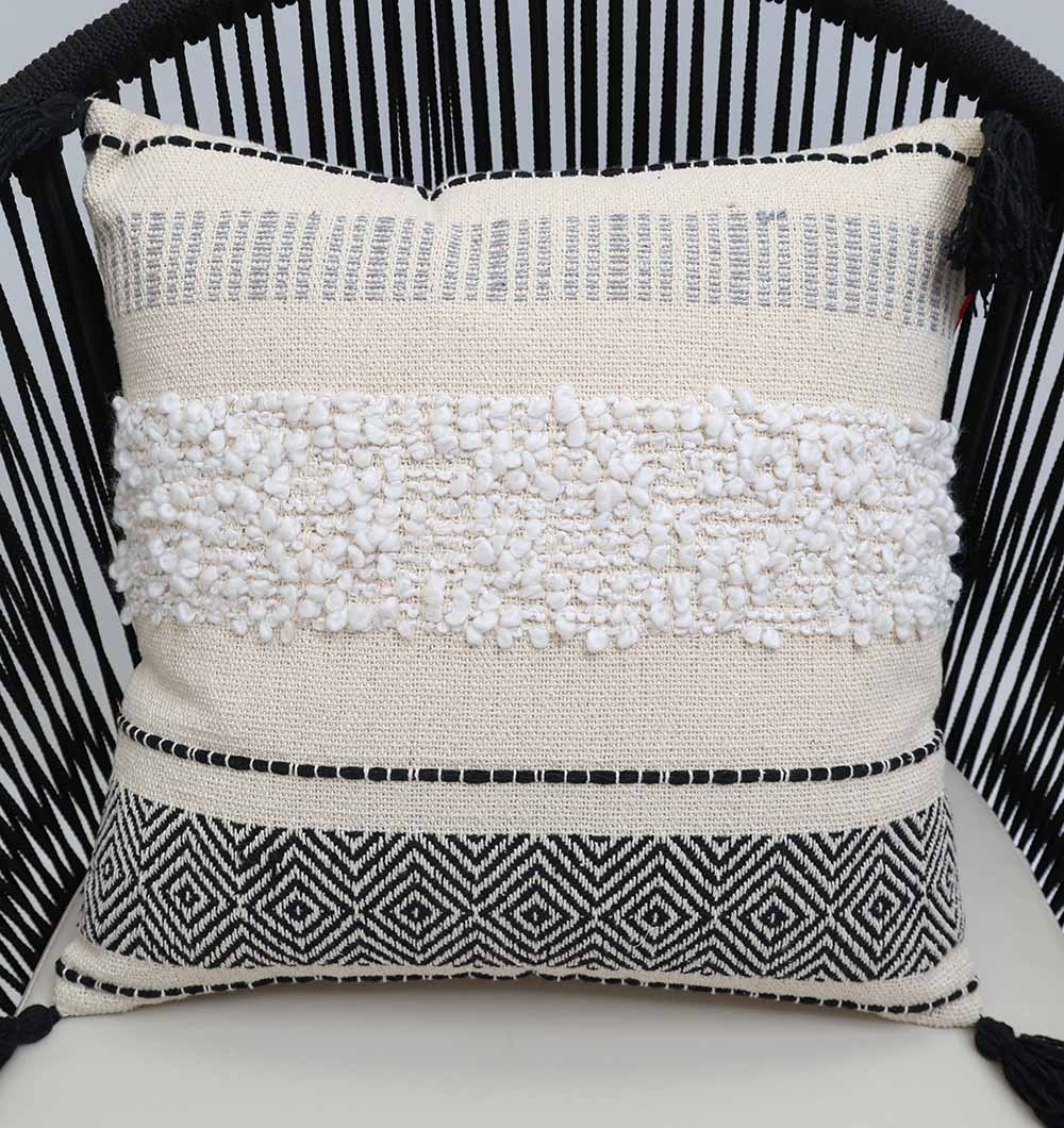 The Multi Color Home Decor Cushion - CS 314 C by Ramsha Home features a cream cotton base, textured white center, black geometric color blocking, and fine black top stitching, displayed on a black slatted chair.