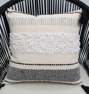 The Multi Color Home Decor Cushion - CS 314 C by Ramsha Home features a cream cotton base, textured white center, black geometric color blocking, and fine black top stitching, displayed on a black slatted chair.