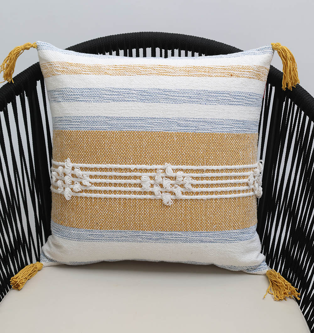 The Multi Color Home Decor Cushion - CS 315 A by Ramsha Home features white, blue, and mustard yellow stripes with white center knots and yellow tassels on each corner, shown on a black woven chair.