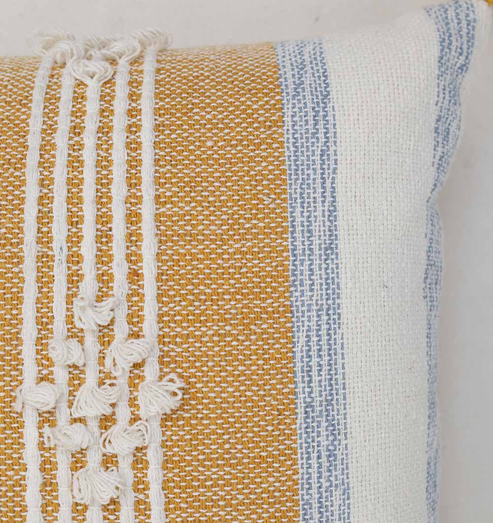 Close-up of the Ramsha Home Multi Color Home Decor Cushion - CS 315 A, featuring mustard yellow, white, and light blue stripes with textured white embroidery, decorative top tassels, and a visibly coarse weave.