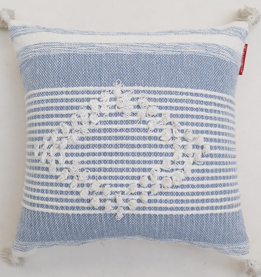 The Ramsha Home Multi Color Home Decor Cushion - CS 315 B features blue and white woven stripes, an oval tufted embroidery in the center, corner tassels, and a small red tag—perfect for adding elegance to your living space.