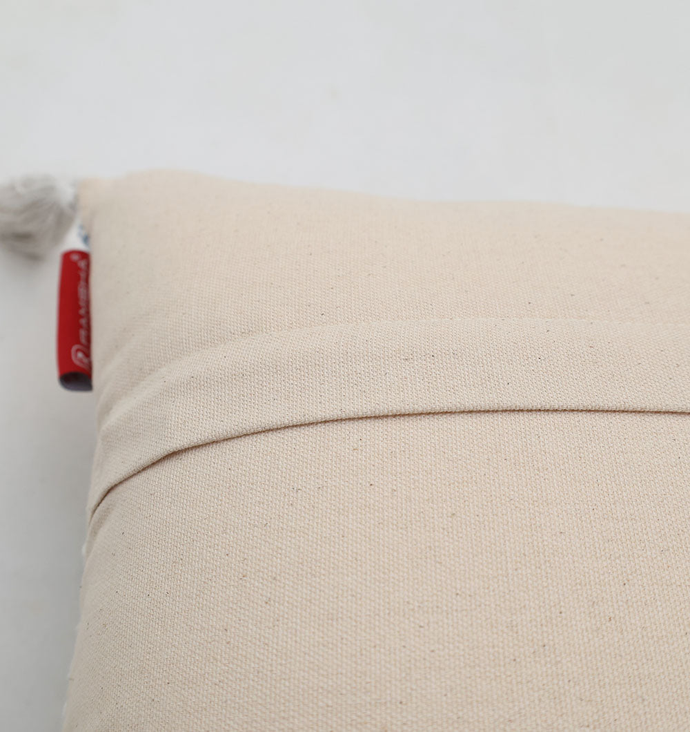 A close-up of the Multi Color Home Decor Cushion - CS 315 B by Ramsha Home, showing a beige color block design, pocket-style back, small red side tag, and a decorative tassel in the upper left corner against a plain light background.