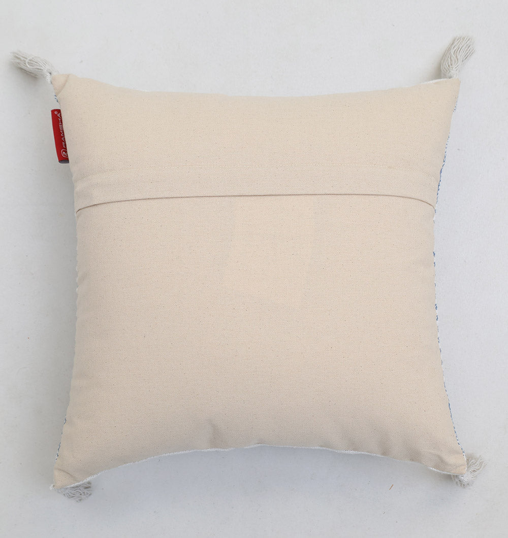 The Multi Color Home Decor Cushion - CS 315 B by Ramsha Home features a square beige cotton design with decorative tassels on each corner, a pocket-style back, and a red fabric tag visible on the left side, resting on a neutral surface.