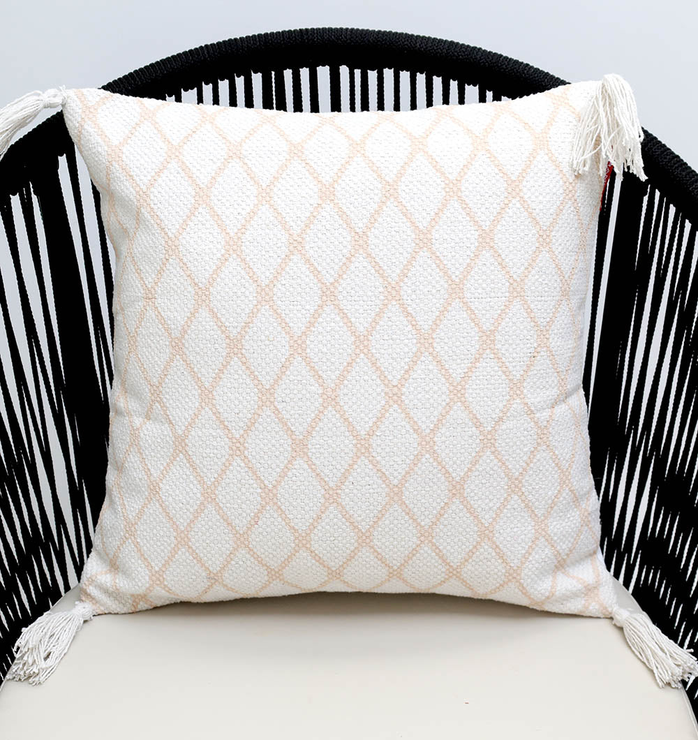 The White and Peach Color Cushion 45x45 cm CS 316 by Ramsha Home, a luxury rugs & home furnishings brand in the UAE, features a light beige diamond pattern with tasseled corners, shown here on a black woven chair with curved slats.