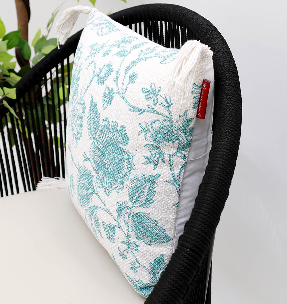 The Blue Color Floral Print Cotton Cushion 45x45 cm (CS 317) from Ramsha Home adds elegant charm to your space when placed on a modern black woven chair, perfectly complemented by a leafy plant for a stylish touch.