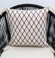 The Cream & Brown Printed Cotton Cushion 45x45 cm CS 318 by Ramsha Home sits on a black, modern slatted chair. The cushion features a cream background, brown diamond lattice pattern, and tassels on each corner.