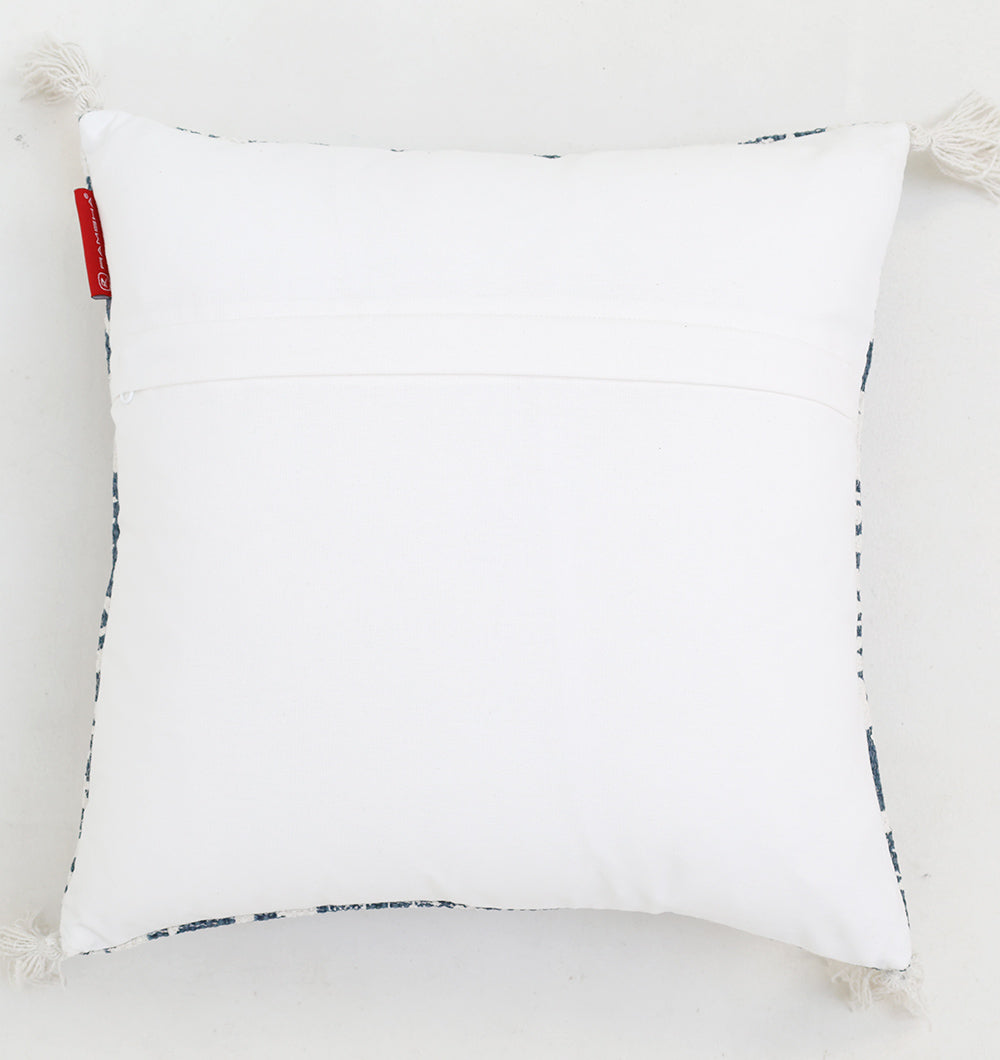 The Ramsha Home White and Blue Printed Cotton Cushion 45x45 cm CS 323 features a stylish design with four corner tassels and a small red fabric tag, shown on a white background.