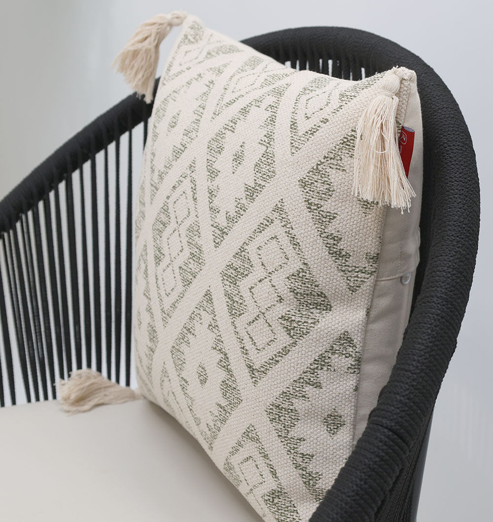 The Ramsha Home White and Grey Printed Cotton Cushion 45x45 cm (CS 325) with geometric design and tasselled corners is displayed on a modern black chair with vertical slats and a light seat.