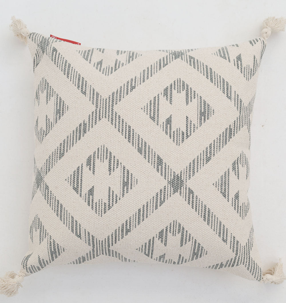 The Ramsha Home Cream and Grey Printed Cotton Cushion 45x45 cm (CS 326) features geometric diamond patterns on a cream background, white tassels at each corner, and a small red tag at the top left. Photographed on a white surface.