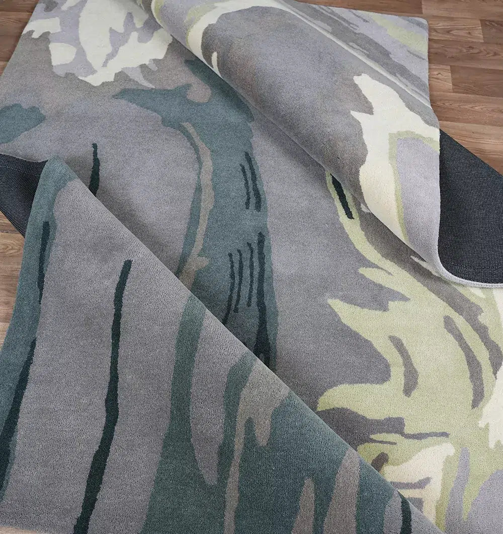 The RAMSHA HOME Beautiful Hand-Tufted Rug - CWL 11 (200x300cm) features an abstract pattern in grey, green, and yellow. Partially rolled up on a wooden floor, it reveals its soft texture and flowing shapes.