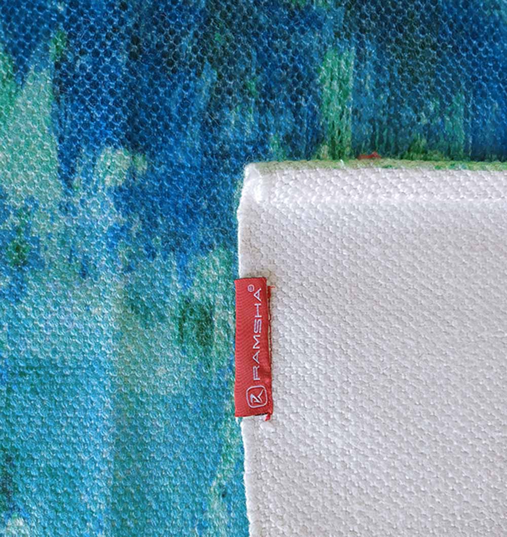 A close-up of the Gradient Printed Durry Multi Color DD-012 by RAMSHA HOME, featuring blue and green textures, partially covered by a folded white fabric with a red “RAMSHA HOME” tag sewn on the edge.