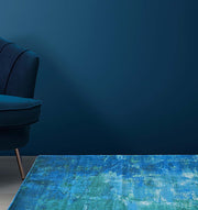 A modern interior scene with a deep blue armchair on the left, the RAMSHA HOME Gradient Printed Durry Multi Color DD-012 rug on the floor in blue and green, and a smooth dark blue wall in the background.