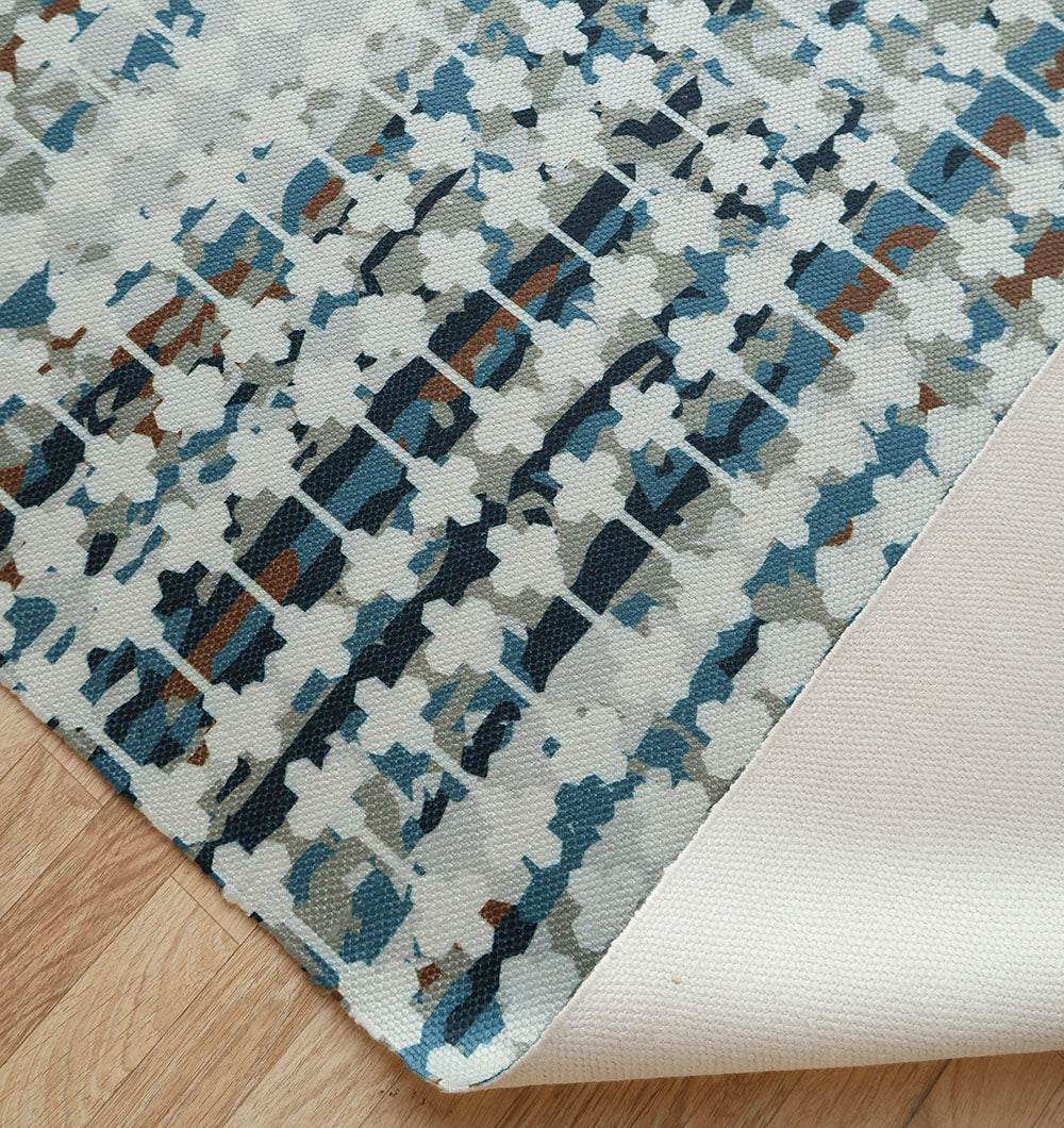 A corner of the RAMSHA HOME Modern Mosaic Digital Printed Rug for Living Room DD-047 is lifted, showing its non-slip backing. The rug, with blue, gray, and brown abstract patterns, lies stylishly on a light wooden floor.