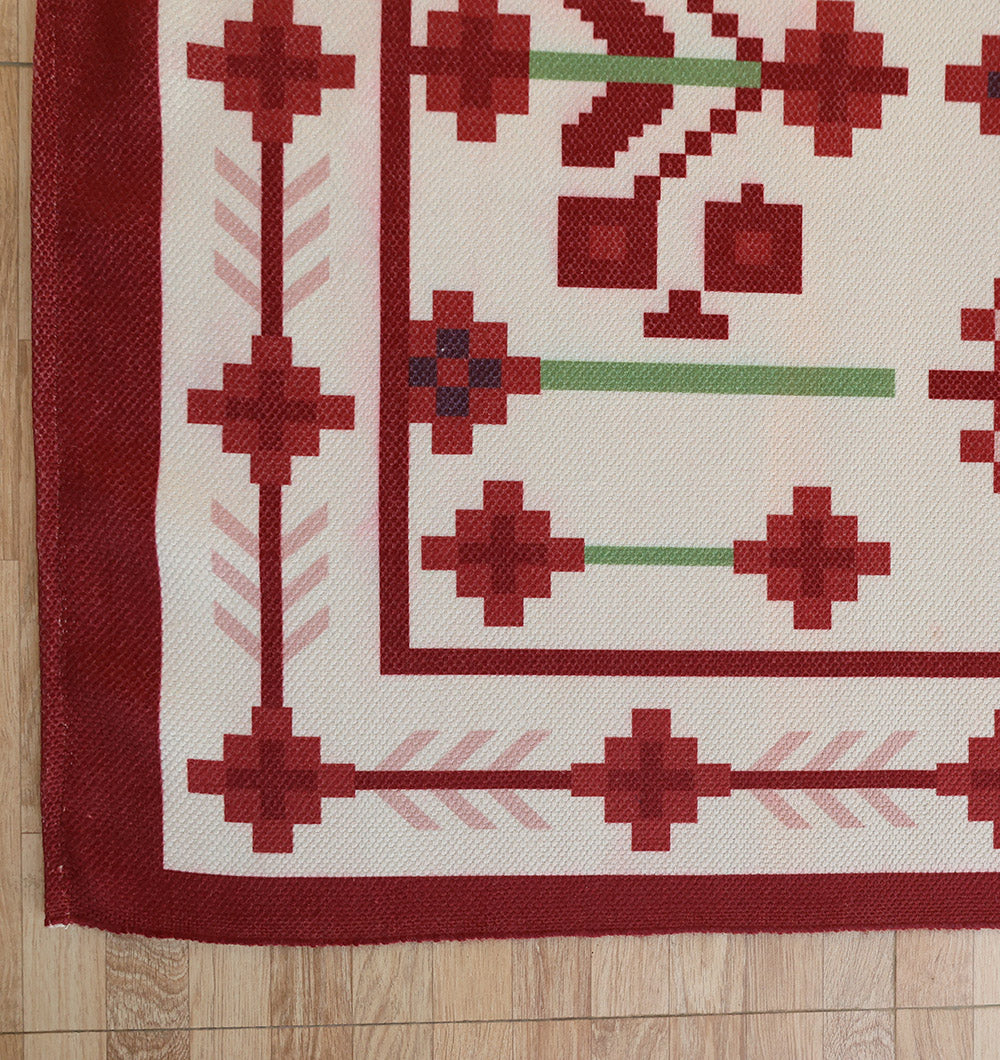 A close-up of the RAMSHA HOME Traditional Red Floral Digital Printed Rug – Bohemian Area Rug DD-048, featuring a red and white geometric pattern with squares, crosses, a red border, and decorative motifs on a wooden floor.