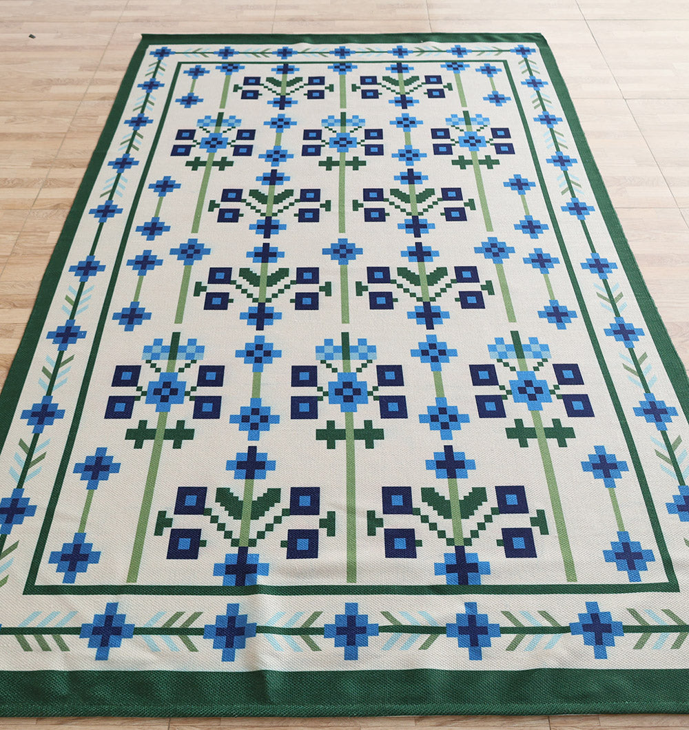 The RAMSHA HOME Blue Traditional Floral Digital Printed Rug – Bohemian Area Rug DD-049 features a beige base with blue, dark blue, and green geometric floral motifs and a green border, shown on a wooden floor.