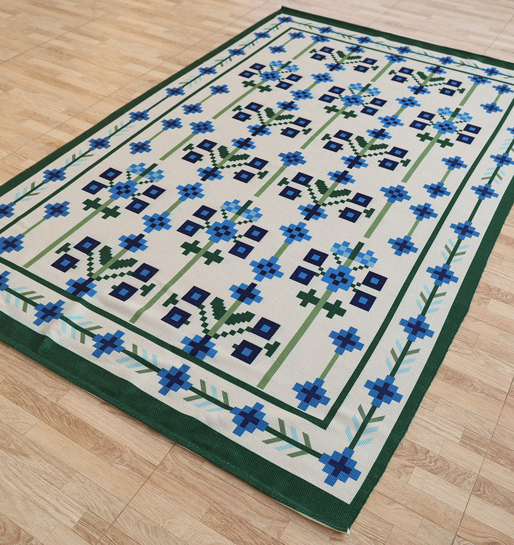 The RAMSHA HOME Blue Traditional Floral Digital Printed Rug – Bohemian Area Rug DD-049 adds Scandinavian style with its pixel-like blue and navy flowers, green stems, and cream background framed in green—perfect on a light wood floor.