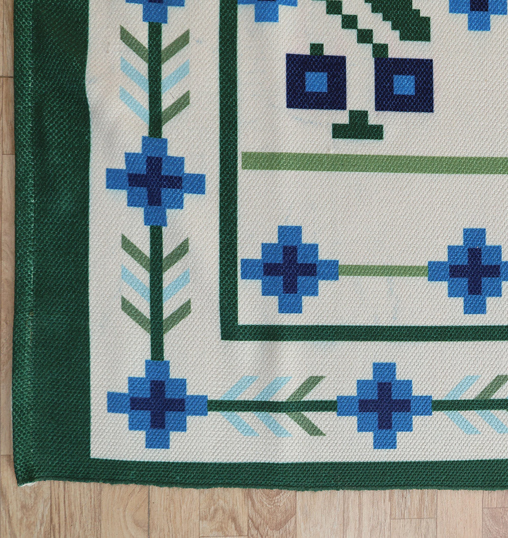 A section of the RAMSHA HOME Blue Traditional Floral Digital Printed Rug – Bohemian Area Rug DD-049 features green borders and blue floral patterns on cream, shown on a light wood floor.