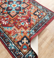 The RAMSHA HOME Bohemian Floral Medallion Printed Area Rug DD-050, featuring vibrant red, blue, orange, and teal geometric and floral patterns, lies on a light wood floor with one corner slightly folded upward.
