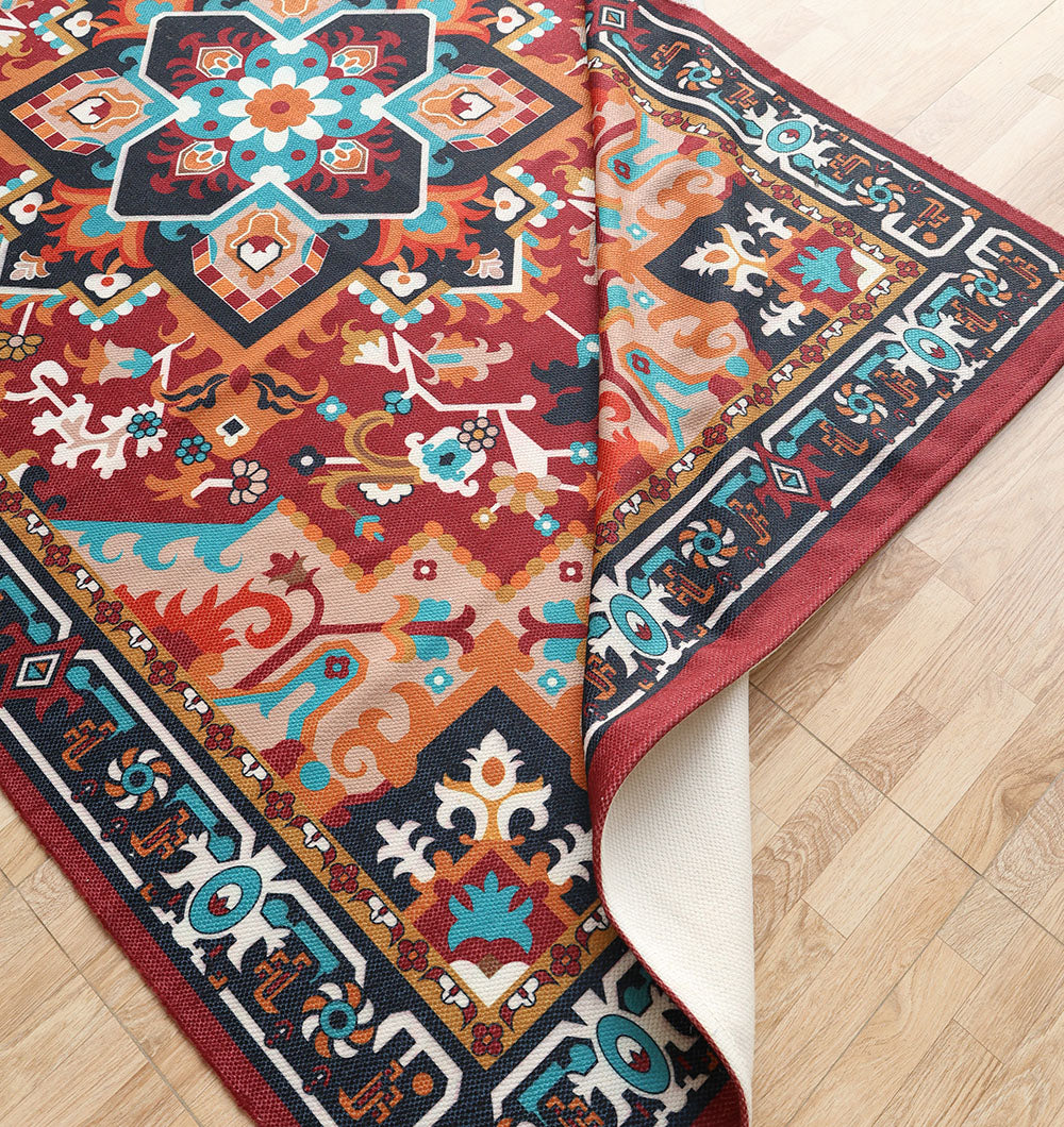 The RAMSHA HOME Bohemian Floral Medallion Printed Area Rug DD-050, featuring vibrant red, blue, orange, and teal geometric and floral patterns, lies on a light wood floor with one corner slightly folded upward.