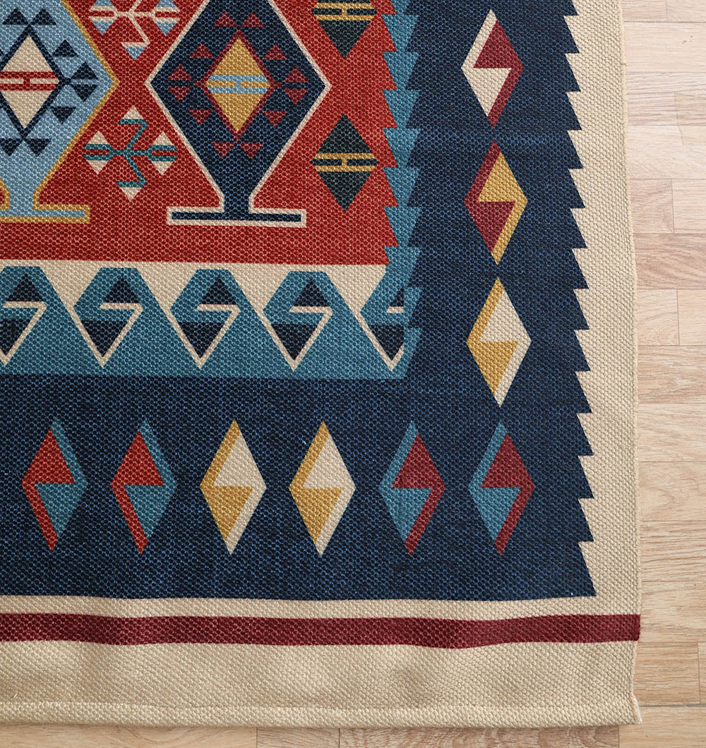 A close-up of the RAMSHA HOME Classic Heritage 145x240 cm Digital Printed Area Rug DD-051, featuring geometric red, blue, beige, and yellow patterns with zigzags and diamonds, shown on a light wooden floor.