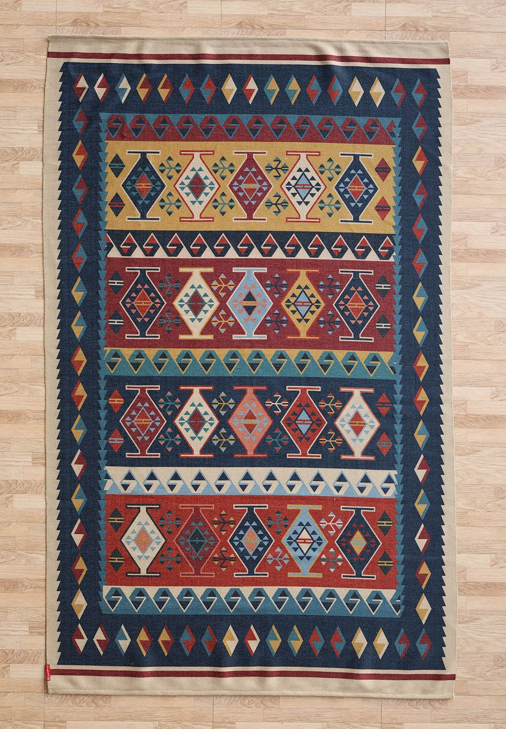 The RAMSHA HOME Classic Heritage 145x240 cm Digital Printed Area Rug DD-051 features geometric patterns with rows of vase-like shapes in red, blue, yellow, and white, bordered by diamond motifs, shown on a light wood floor.