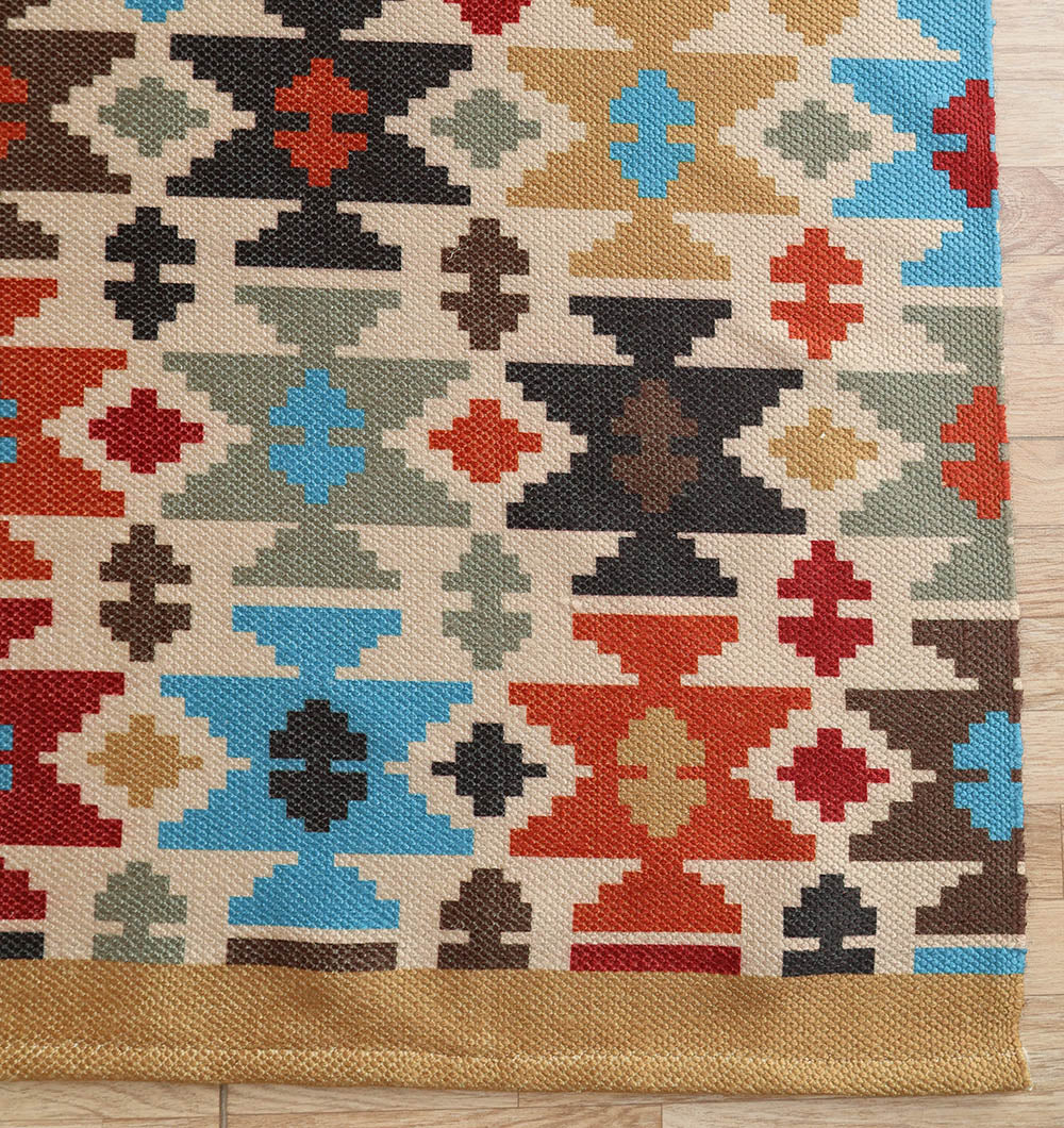 The RAMSHA HOME Tribal Mosaic Digital Printed Rug 145x240 cm DD-052, featuring rows of geometric diamond and cross patterns in red, black, blue, green, brown, and beige, is displayed on a wooden floor.