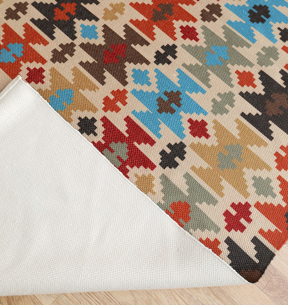 The RAMSHA HOME Tribal Mosaic Digital Printed Rug 145x240 cm (DD-052) features geometric patterns in red, blue, brown, and beige on a light background; one corner is folded to reveal the plain white underside. Displayed on a light wood floor.