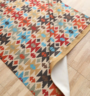The RAMSHA HOME Tribal Mosaic Digital Printed Rug 145x240 cm (DD-052), featuring multicolored geometric designs in red, blue, black, brown, and beige, lies on a light wooden floor with a corner folded to reveal the underside.