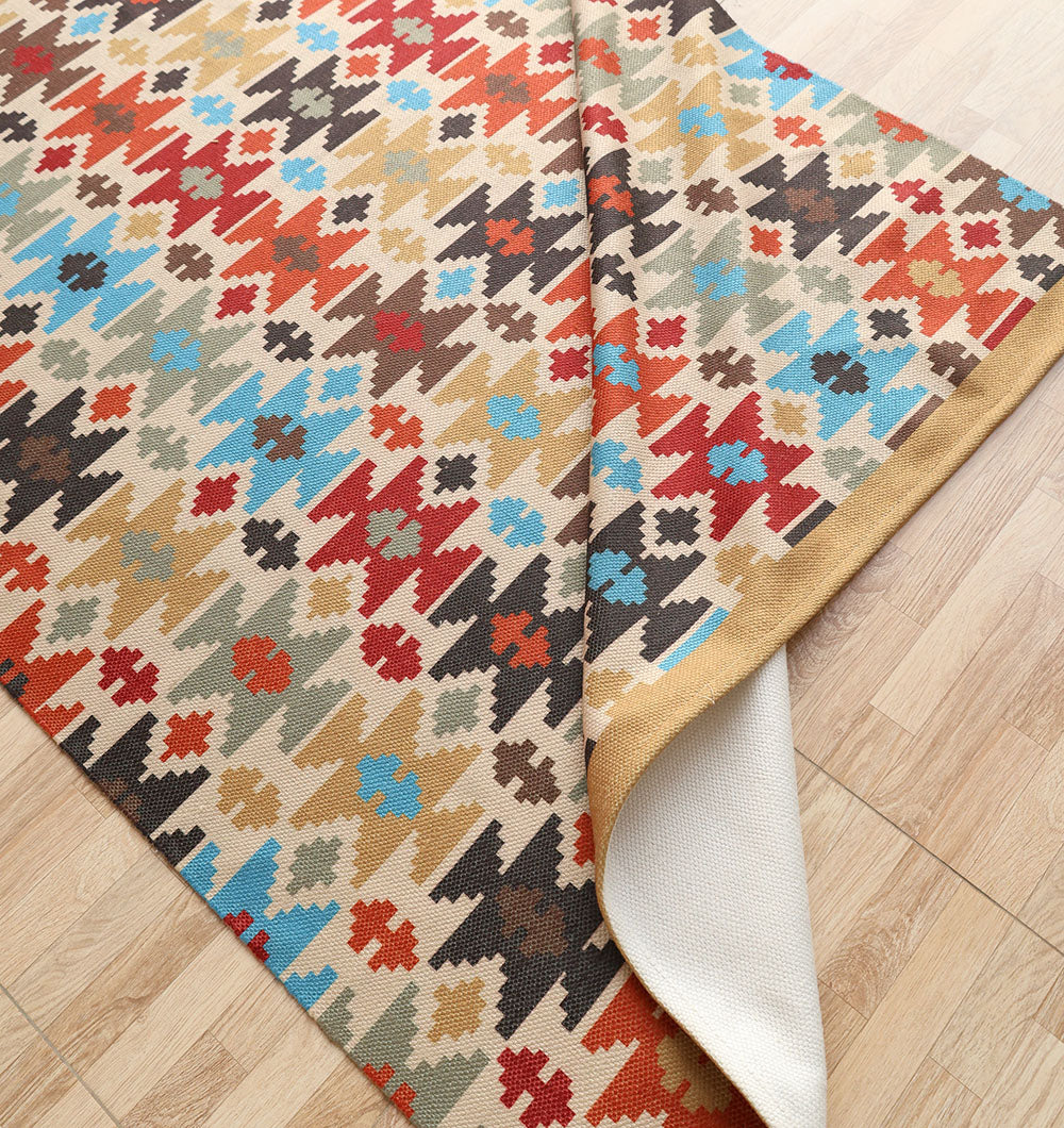 The RAMSHA HOME Tribal Mosaic Digital Printed Rug 145x240 cm (DD-052), featuring multicolored geometric designs in red, blue, black, brown, and beige, lies on a light wooden floor with a corner folded to reveal the underside.