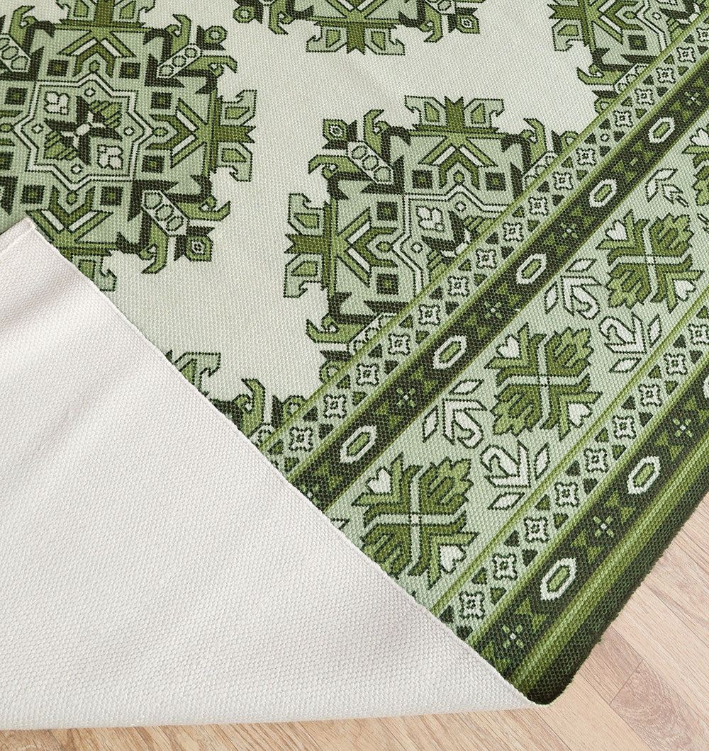 A corner of the RAMSHA HOME Contemporary Tribal Digital Print 145x240 cm Rug DD-053 in green and white geometric patterns is folded over, showing its plain underside, while it lies on a light wood floor.