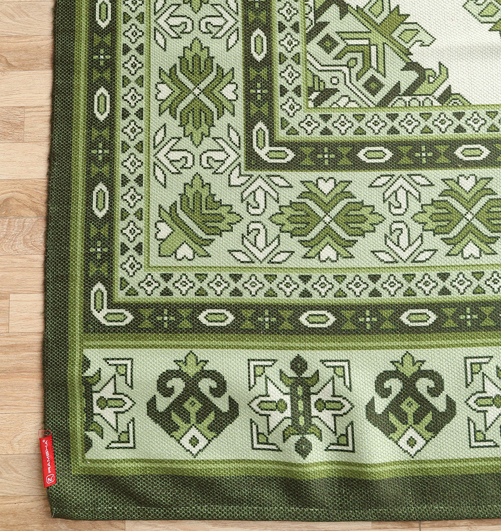 The RAMSHA HOME Contemporary Tribal Digital Print Rug (145x240 cm, DD-053), featuring green and white geometric and floral patterns, lies on a light wood floor with a small red fabric tag on one corner.