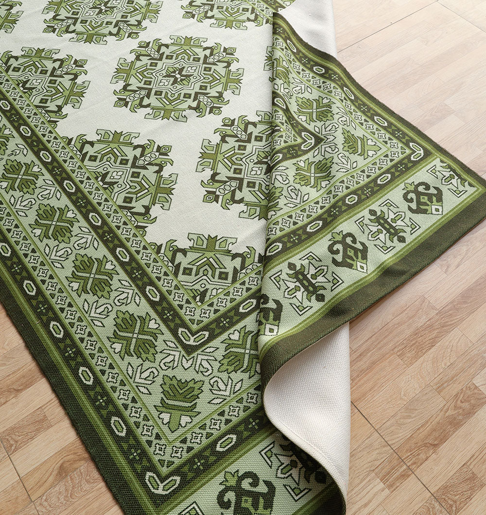 The RAMSHA HOME Contemporary Tribal Digital Print Rug (145x240 cm, DD-053) in green and white, featuring intricate geometric and floral patterns, is partially folded on a light wood floor to show its underside.