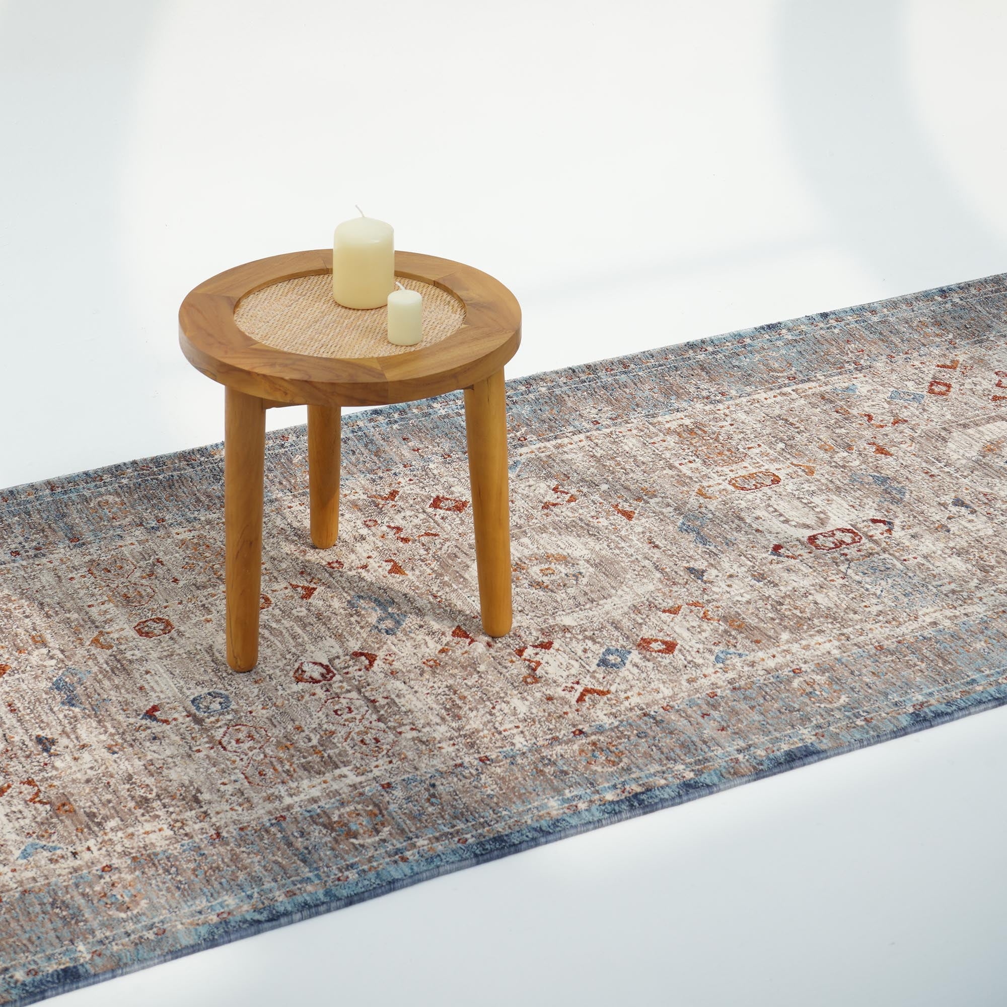 A small round wooden table with two candles sits on the RAMSHA HOME Polyester K860A Area Rug, featuring blue, beige, and rust accents, set against a plain white background.