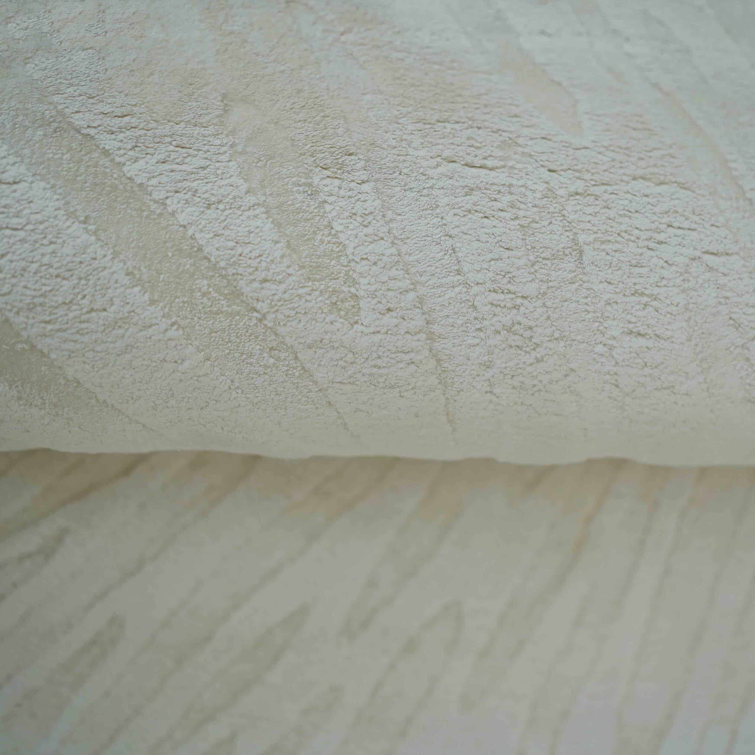 Close-up of the RAMSHA HOME Home Decor Shape Handmade Area Rug - HTV 21, featuring textured off-white fabric with a subtle wavy pattern. The image highlights its soft, slightly raised surface as the rug is folded over itself.