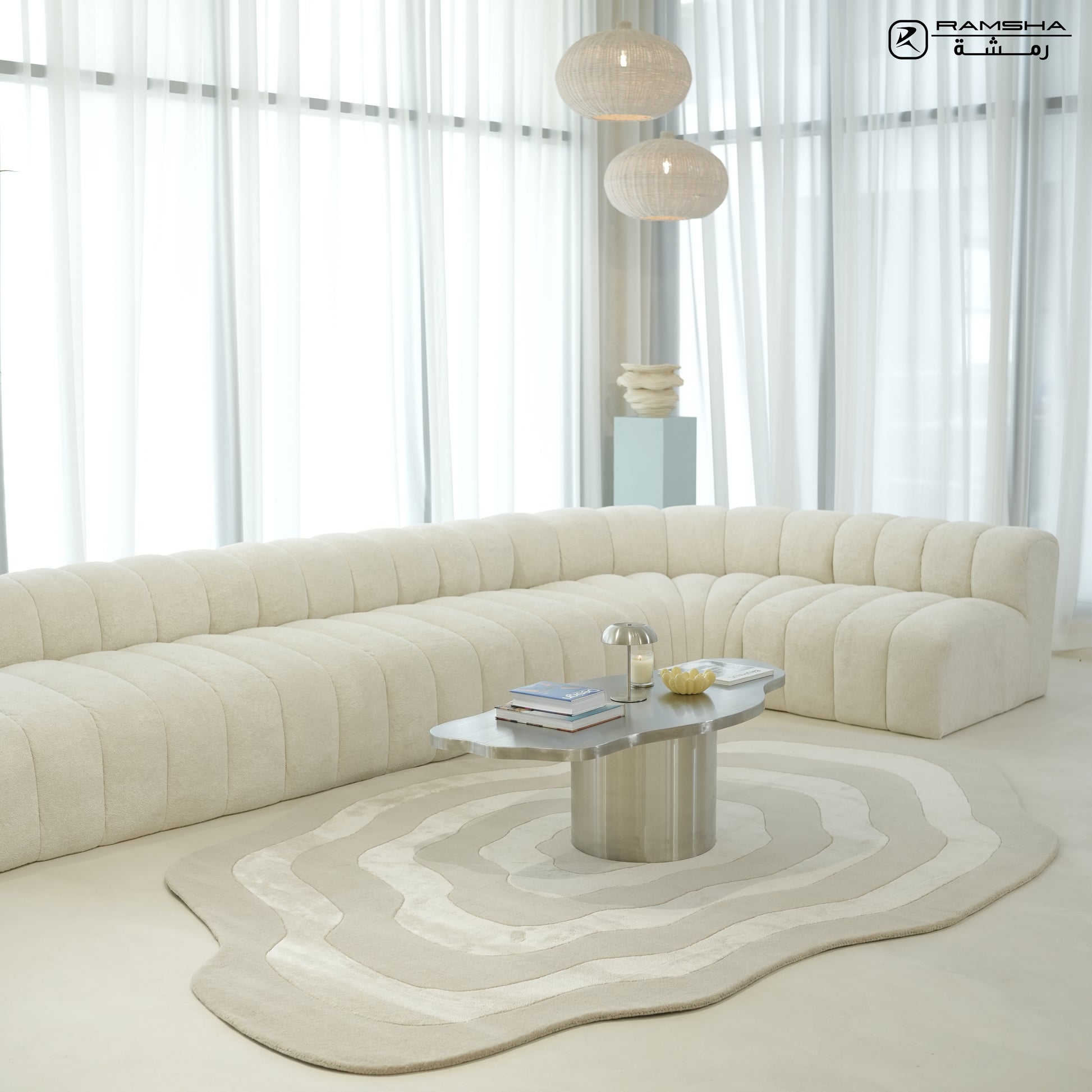A modern living room with a curved, cream-colored sofa, metallic coffee table, globe pendant lights, tall sheer white curtains, and the RAMSHA HOME Wool & Tencel Multi Color Rug HTWV-91.