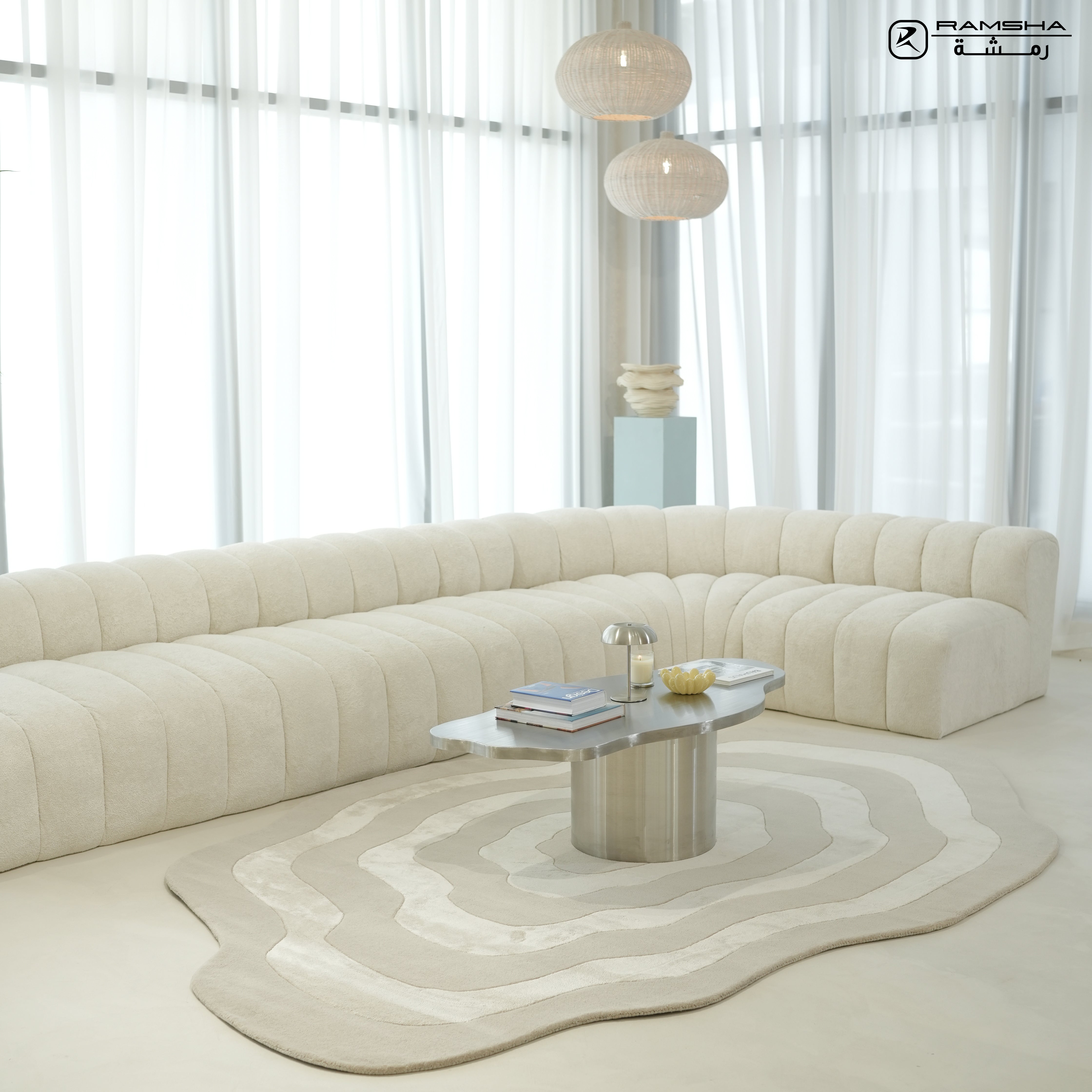 A modern living room with a curved, cream-colored sofa, metallic coffee table, globe pendant lights, tall sheer white curtains, and the RAMSHA HOME Wool & Tencel Multi Color Rug HTWV-91.