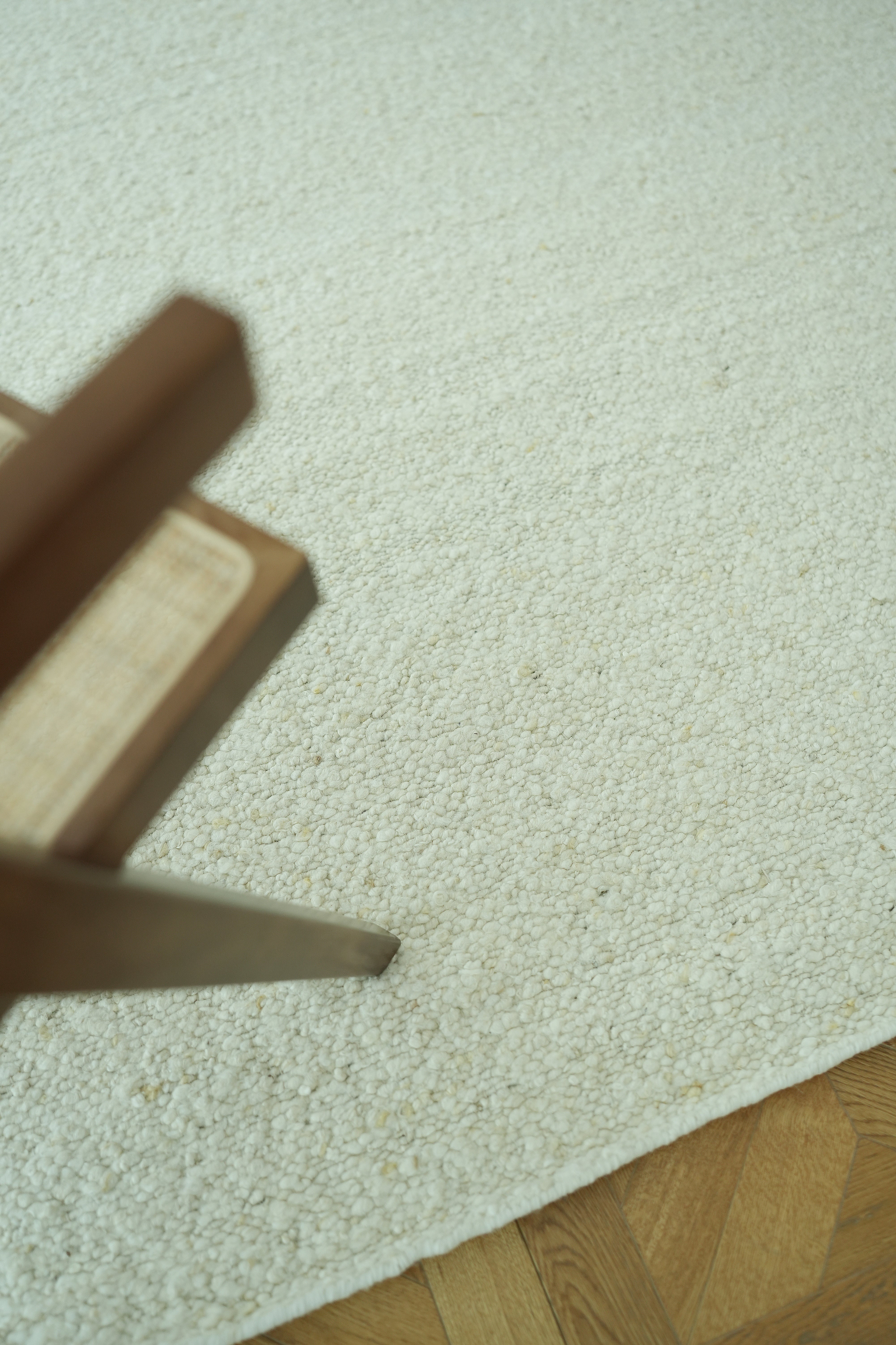A close-up of the RAMSHA HOME Handmade Natural Off White Woven Rug For Home Decor SR-059 on a wooden parquet floor, with a wooden furniture corner visible in the upper left of the image.