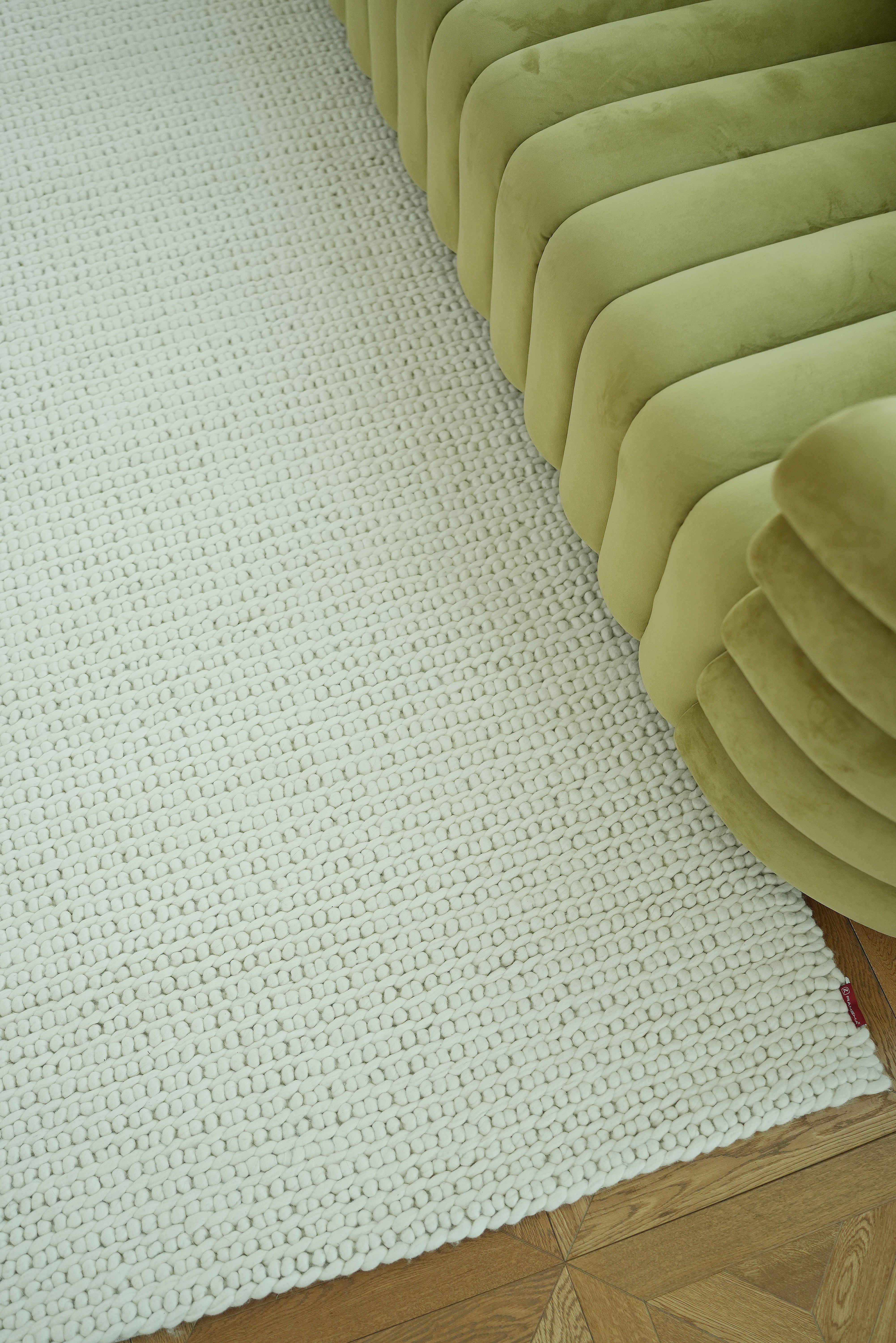 A close-up of a light green velvet tufted sofa beside the Handmade Natural White Woven Rug For Home Decor SRN-031 on a wooden floor, highlighting the rug's elegant texture and cozy ambiance.