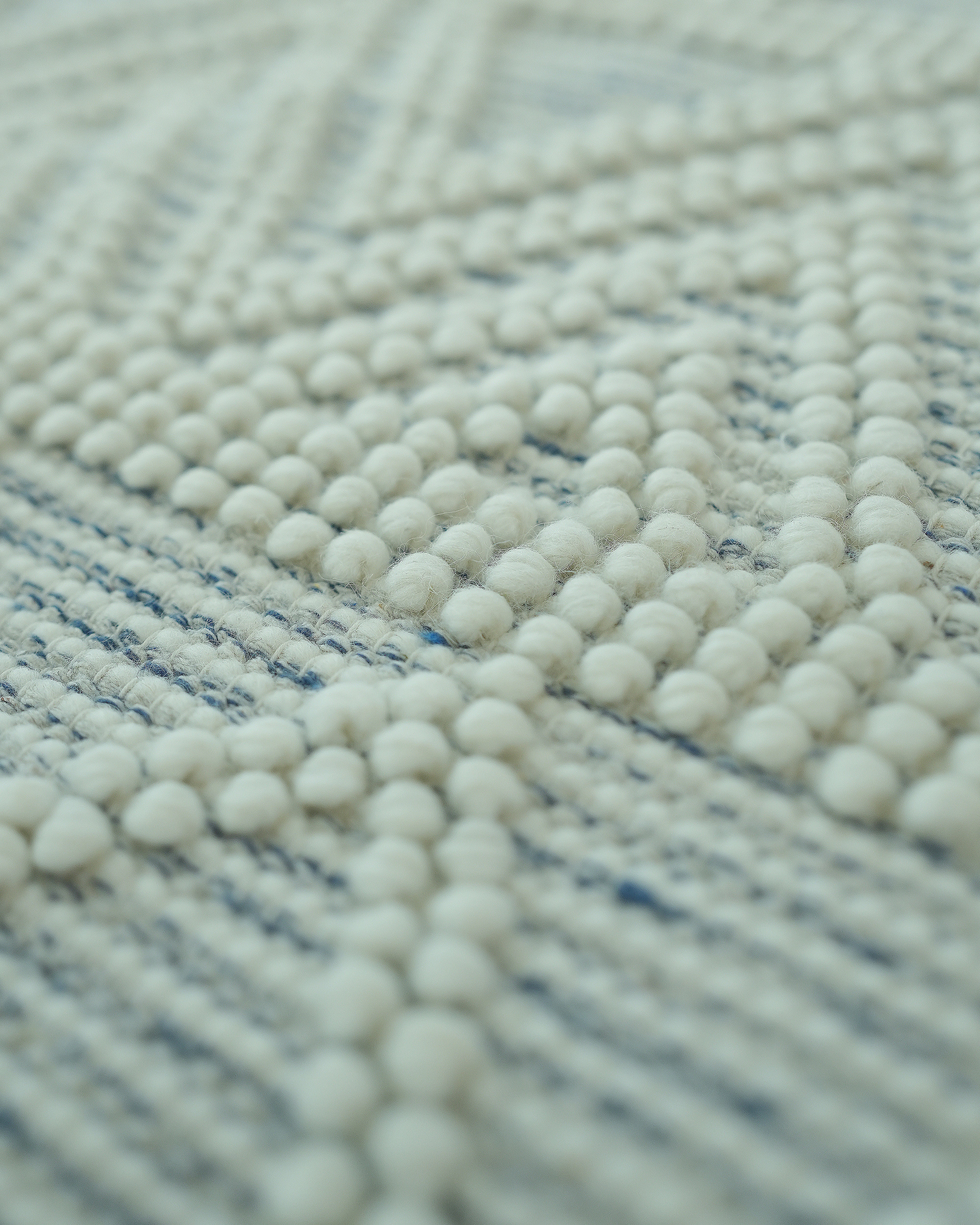 Close-up of RAMSHA HOME’s Handmade Woven Rug SRN-021, featuring a natural and white color palette with geometric patterns and textured round beads. The shallow focus highlights the rug's intricate wool design and craftsmanship.