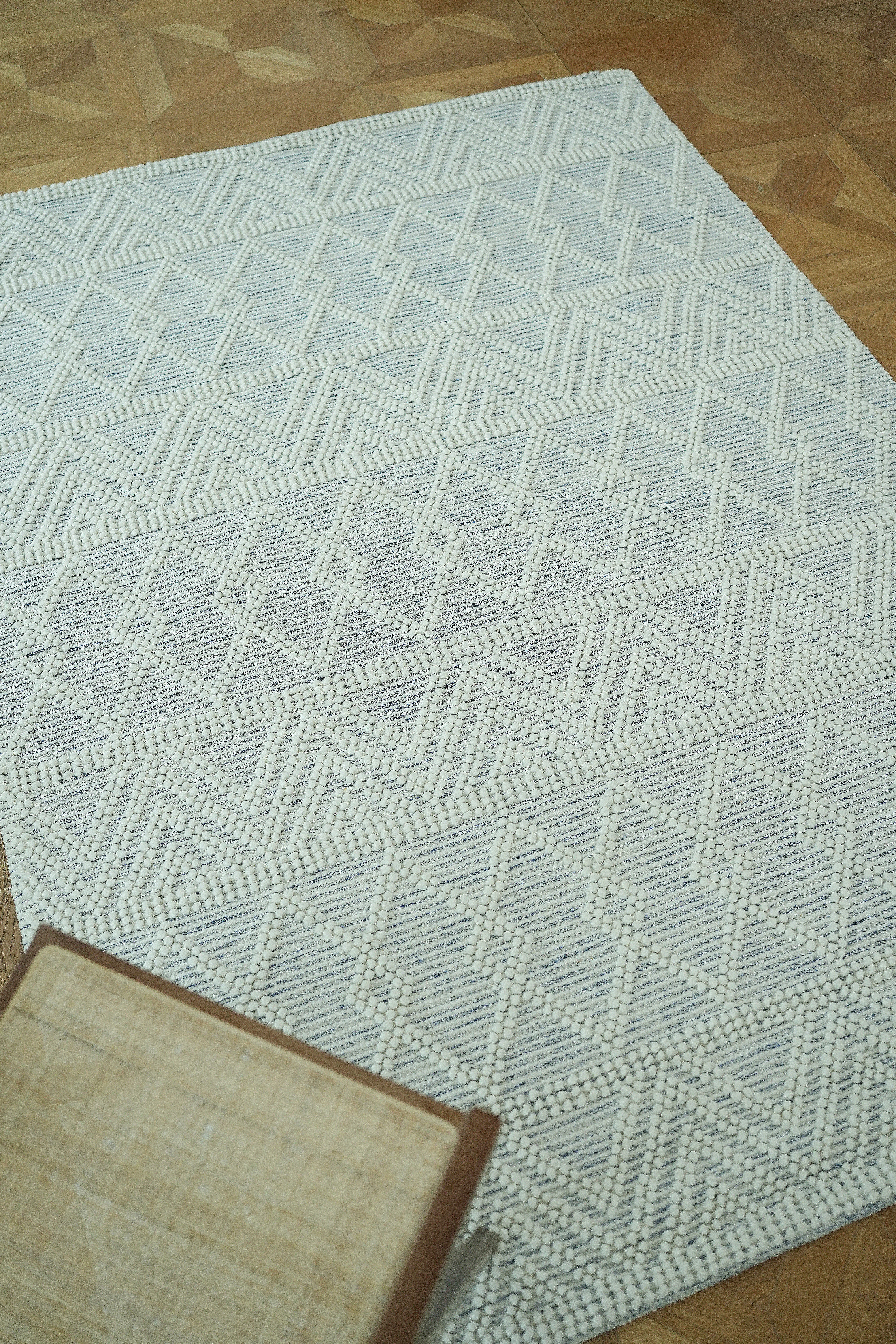 The RAMSHA HOME Handmade Woven Rug Natural & White Color Floor Rug SRN-021 features a white geometric pattern and is displayed on a parquet wood floor, with a small woven stool partially visible in the corner.