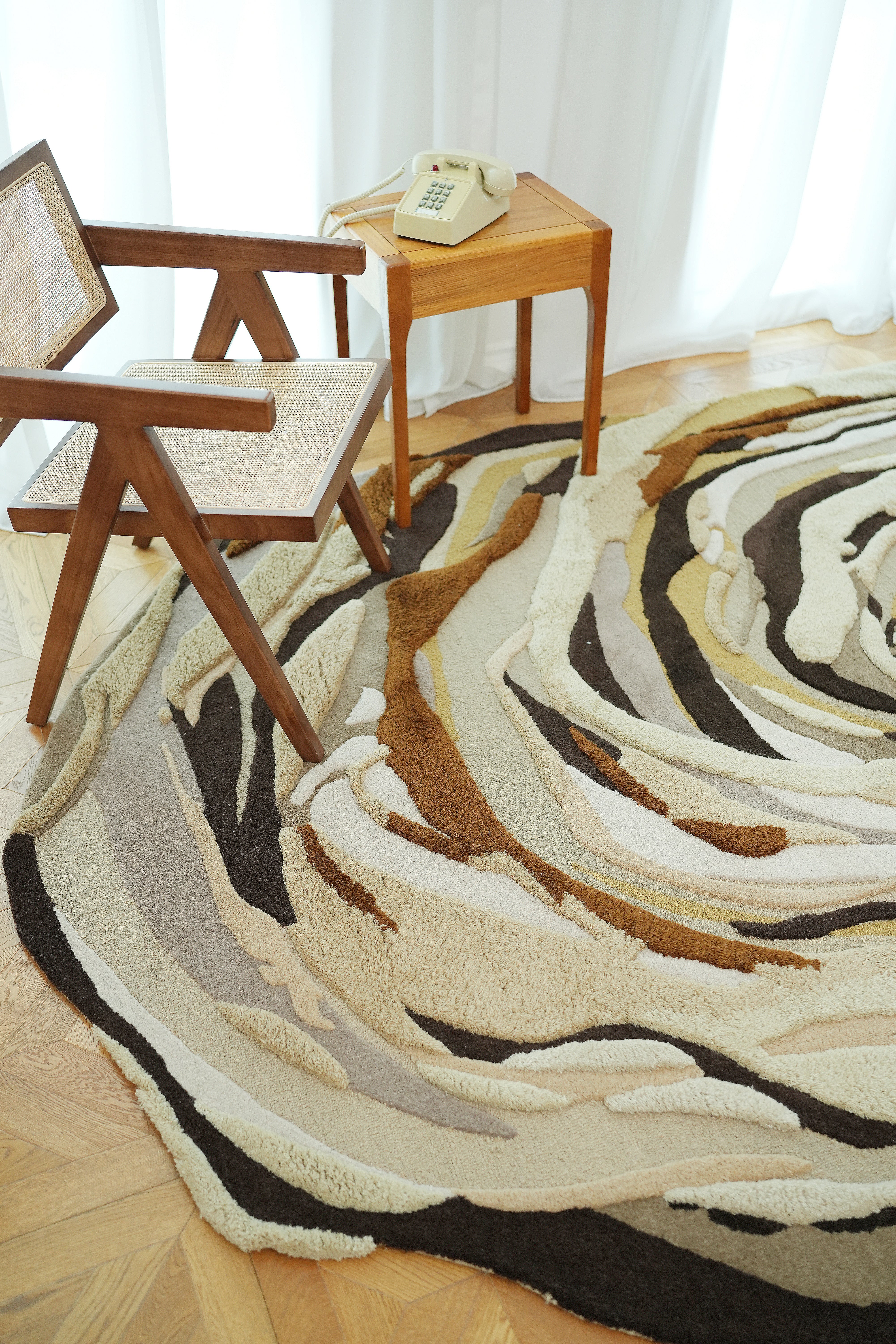 A modern wooden chair and small table with a rotary phone sit on the RAMSHA HOME Handmade Shaped Multicolor Area Rug HTW 126 (200 x 300 cm), near a window with white curtains.