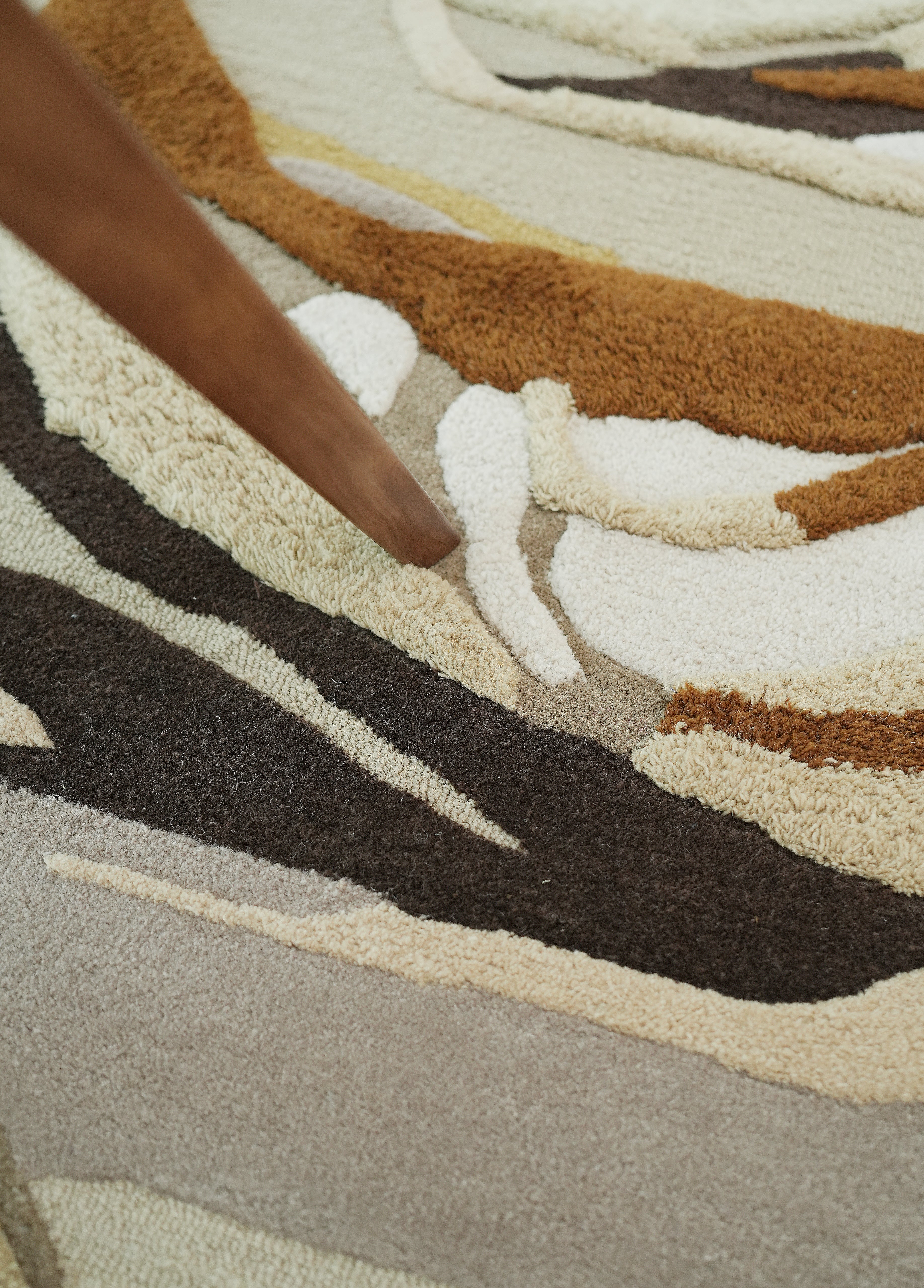 Close-up of the RAMSHA HOME Handmade Shaped Multicolor Area Rug HTW 126 (200 x 300 cm) featuring abstract wavy patterns in brown, tan, beige, cream, and dark brown, with a wooden furniture leg on the modern wool rug.