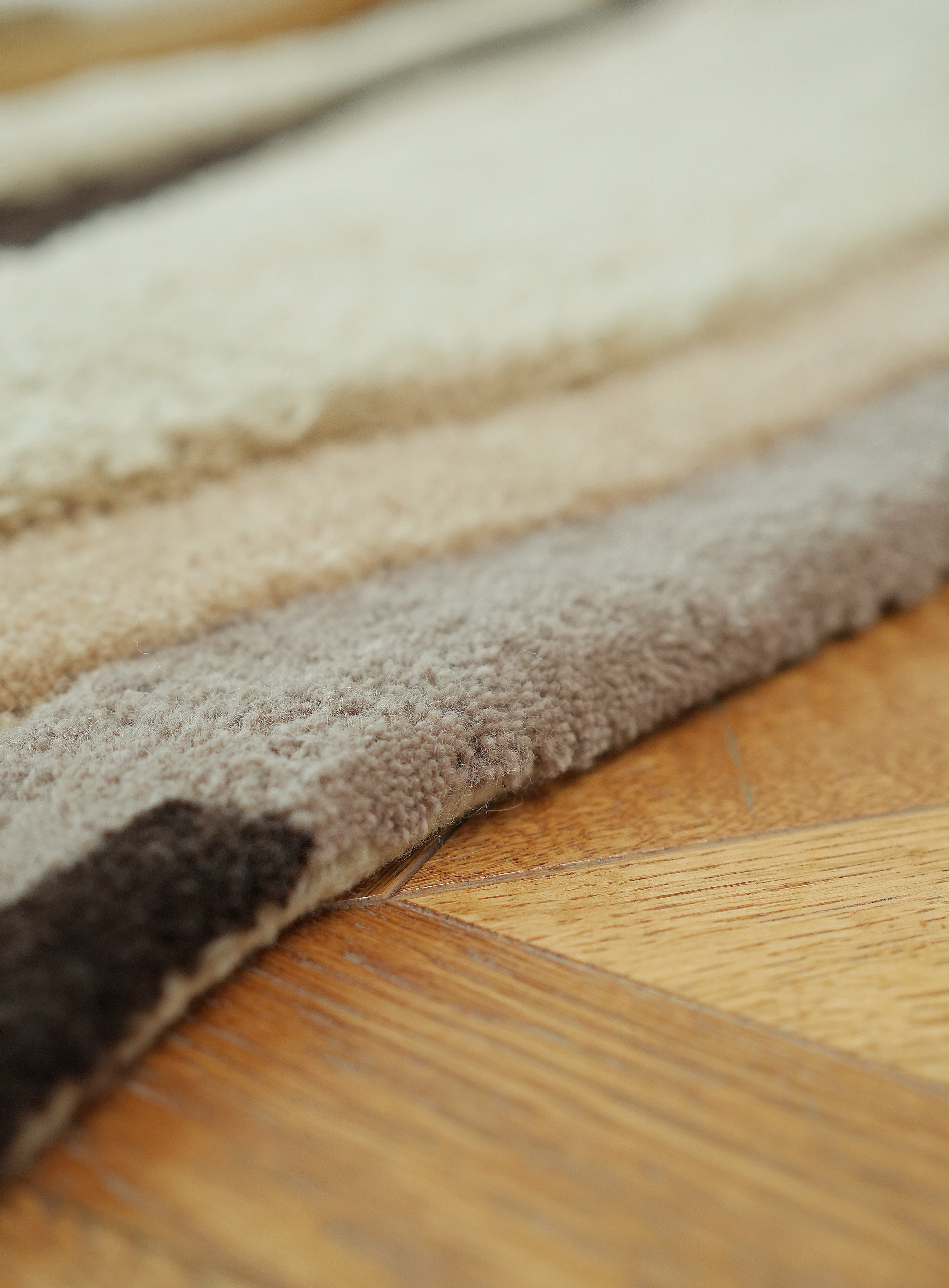 A close-up of the Handmade Shaped Multicolor Area Rug HTW 126 by RAMSHA HOME (200 x 300 cm), featuring cream, beige, and brown stripes, shown on a wooden floor—an ideal neutral accent for any space.
