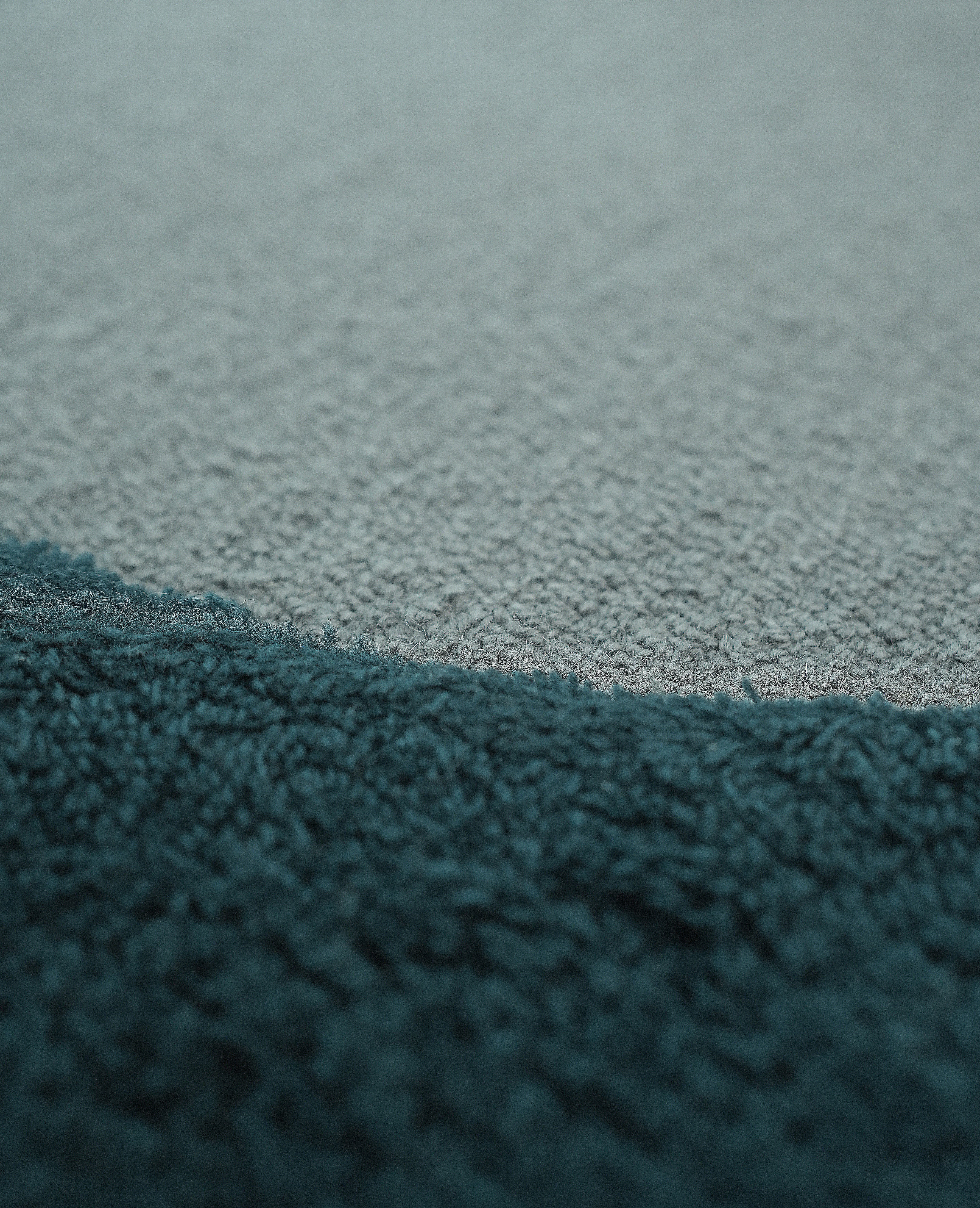 Close-up of RAMSHA HOME's Handmade Layered Abstract Shaped Rug HTW 131 (200 x 300 cm): its soft, fuzzy dark teal surface contrasts with smooth light gray fabric in an irregular modern design.