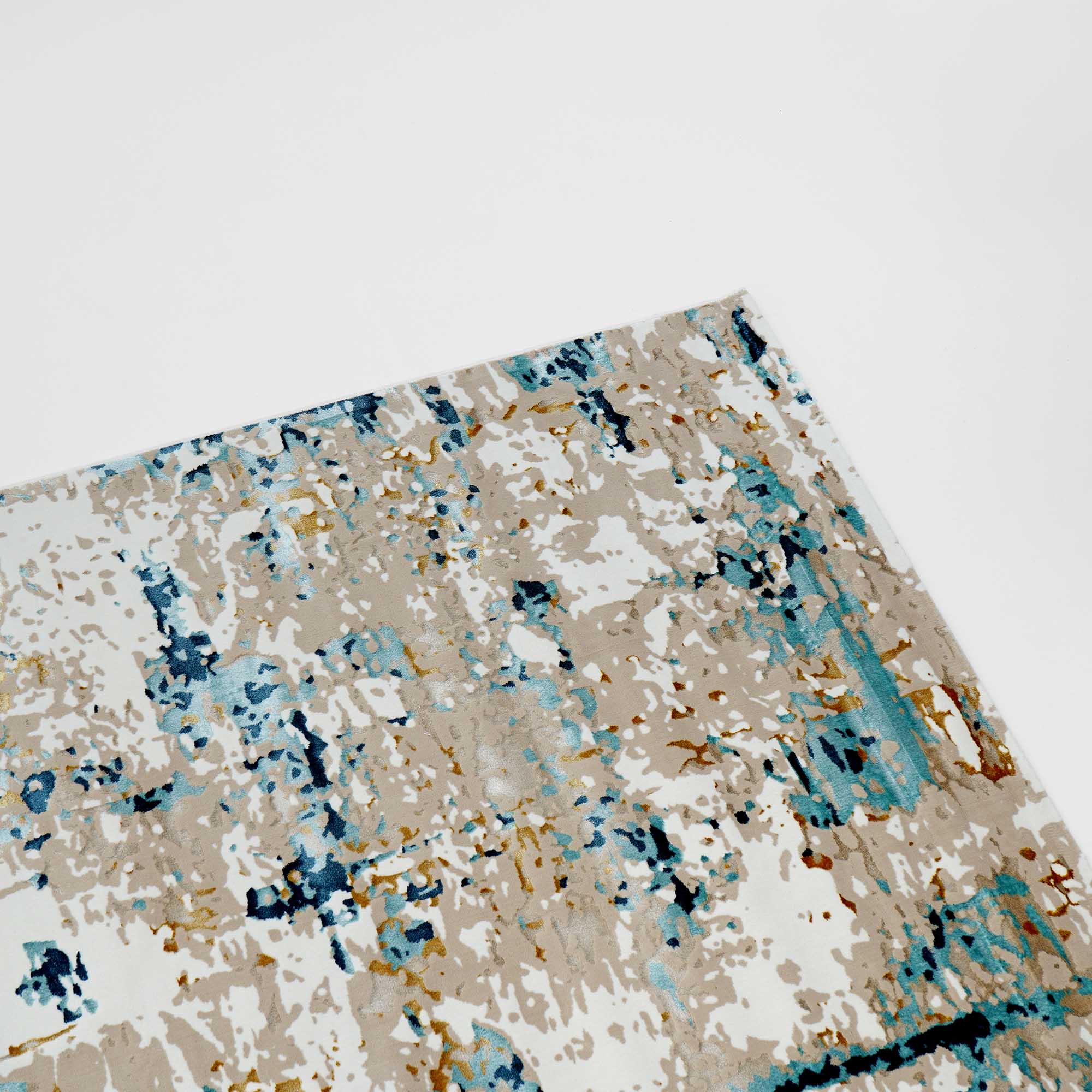 A close-up shows the corner of the RAMSHA HOME Stunning Cream & Blue Color Turkish Machine Made Rug (MZ61B), featuring a modern, stain-resistant abstract pattern in blue, beige, gold, and white on a white background.