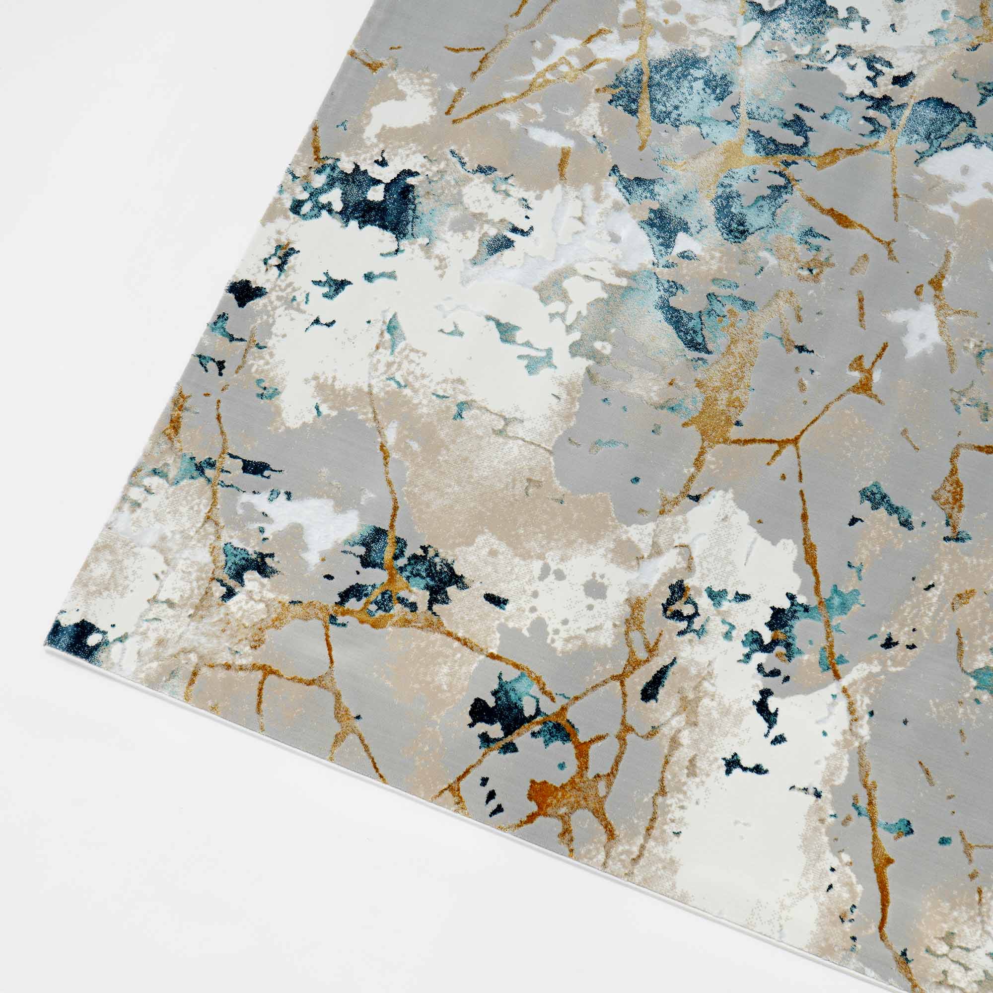 The RAMSHA HOME Cream & Gold Color Machine Made Turkish Rug (NN66A) features a marble-inspired abstract pattern in blue, teal, white, beige, and gold on a light background. Shown angled top-down, this stain-resistant polyester area rug adds modern style.