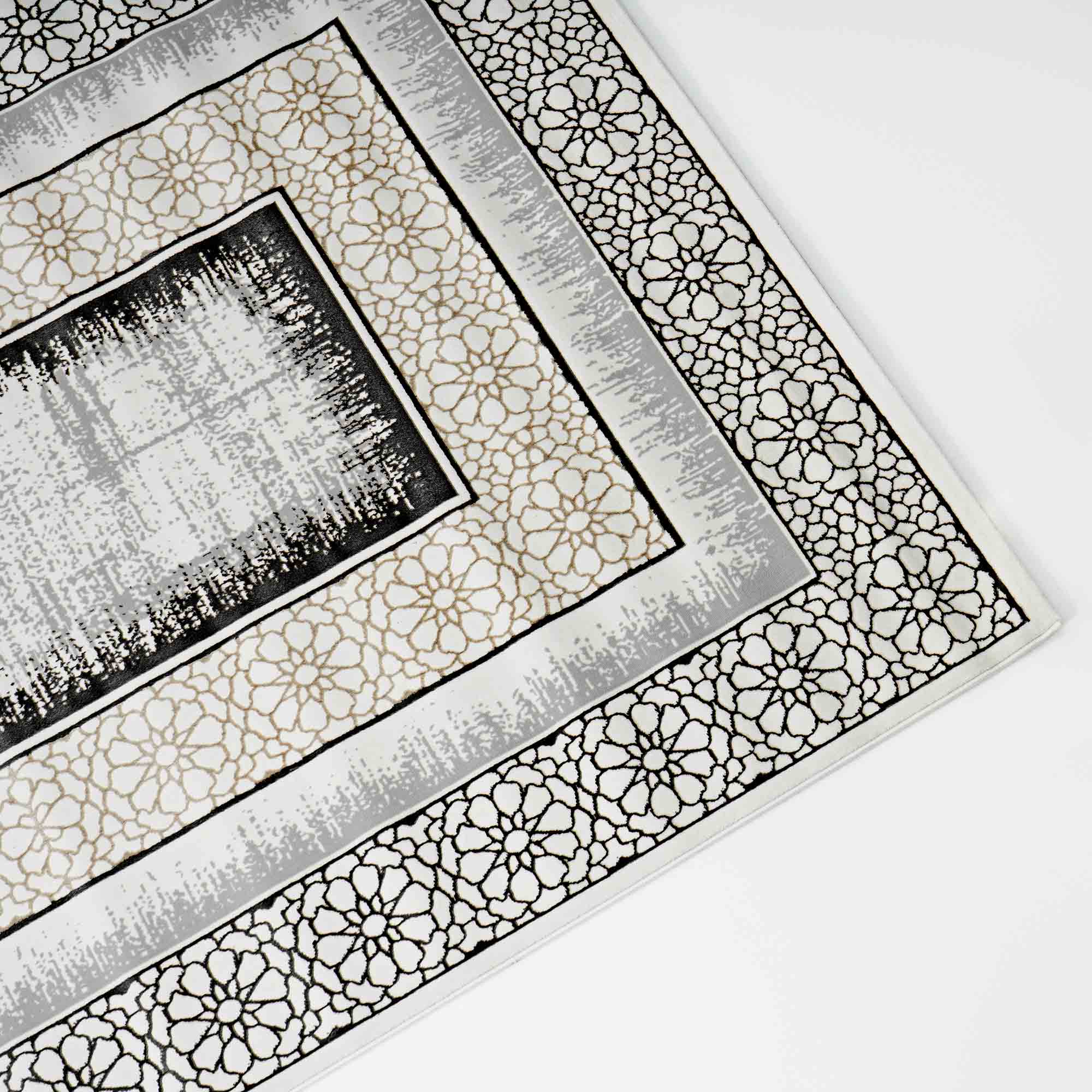 A close-up of the RAMSHA HOME Grey Color ND81A BARCELONA Decor Area Rug, featuring intricate floral and geometric patterns in black and beige on a white background, photographed at an angle against a white surface.