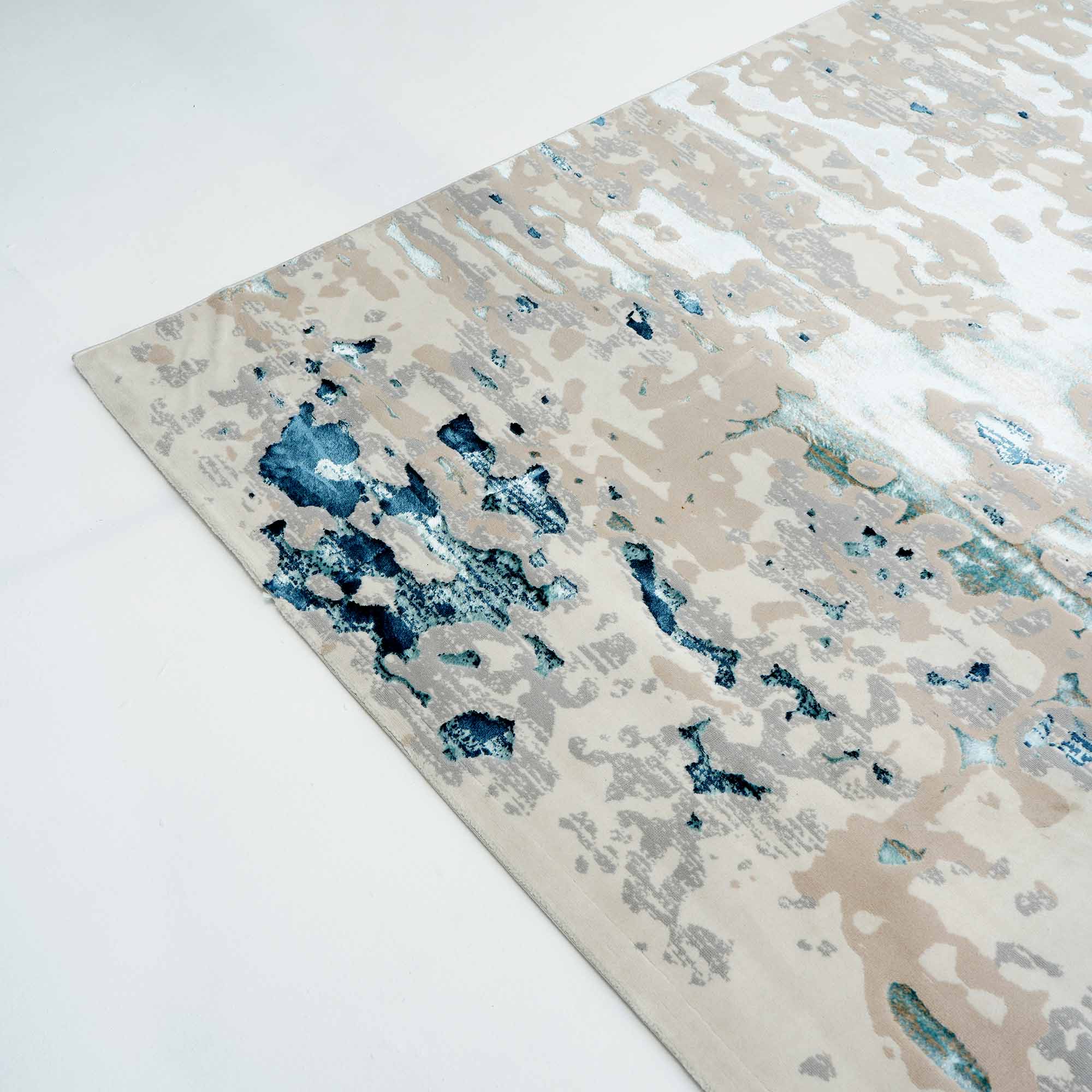 A close-up of the RAMSHA HOME Light Blue Turkey Area Rug NF98B, featuring a modern distressed abstract pattern in beige, white, blue, and grey tones on a white floor.